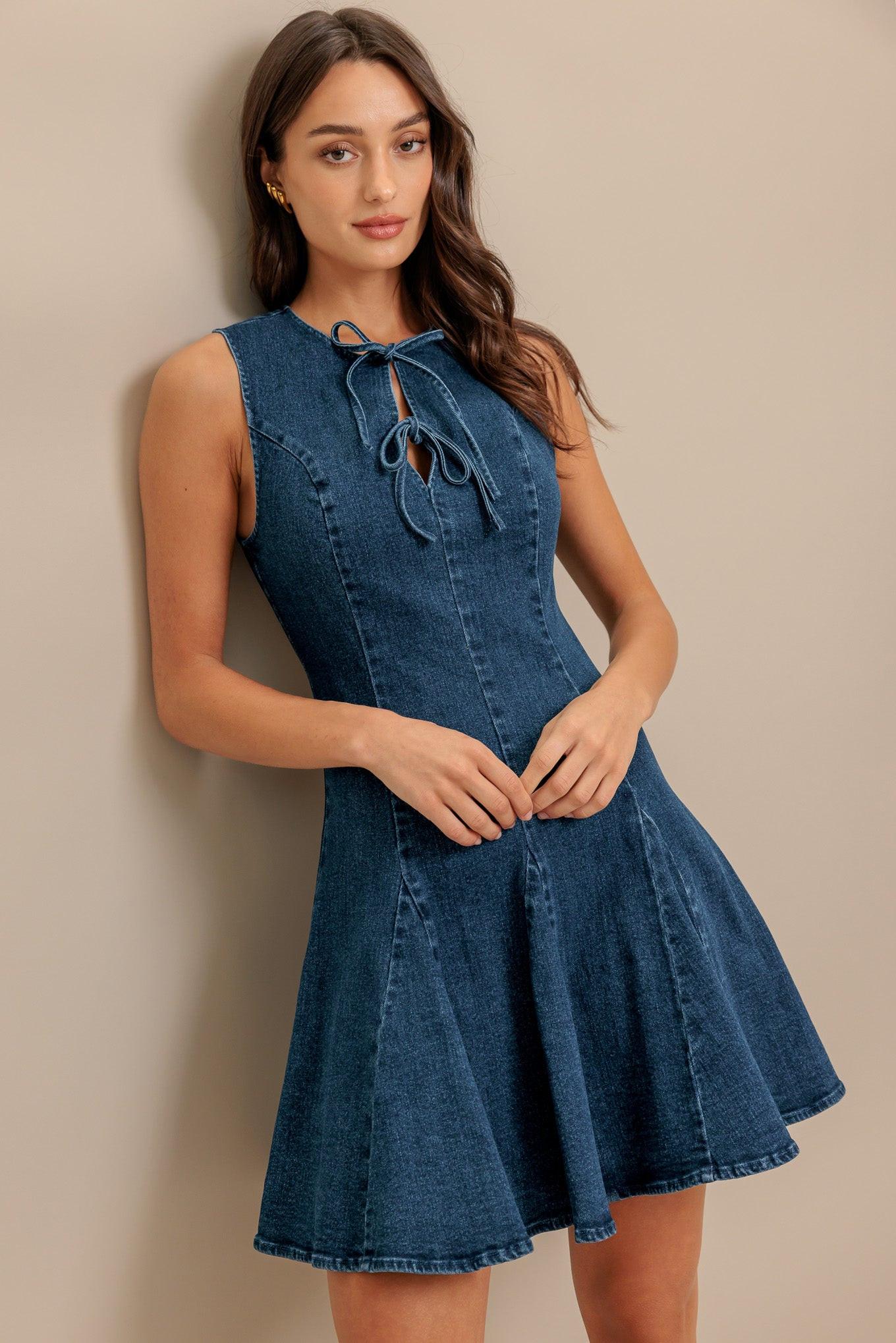 A washed denim mini dress featuring round neckline, sleeveless, front bow ties, circle skirt and back zipper closure