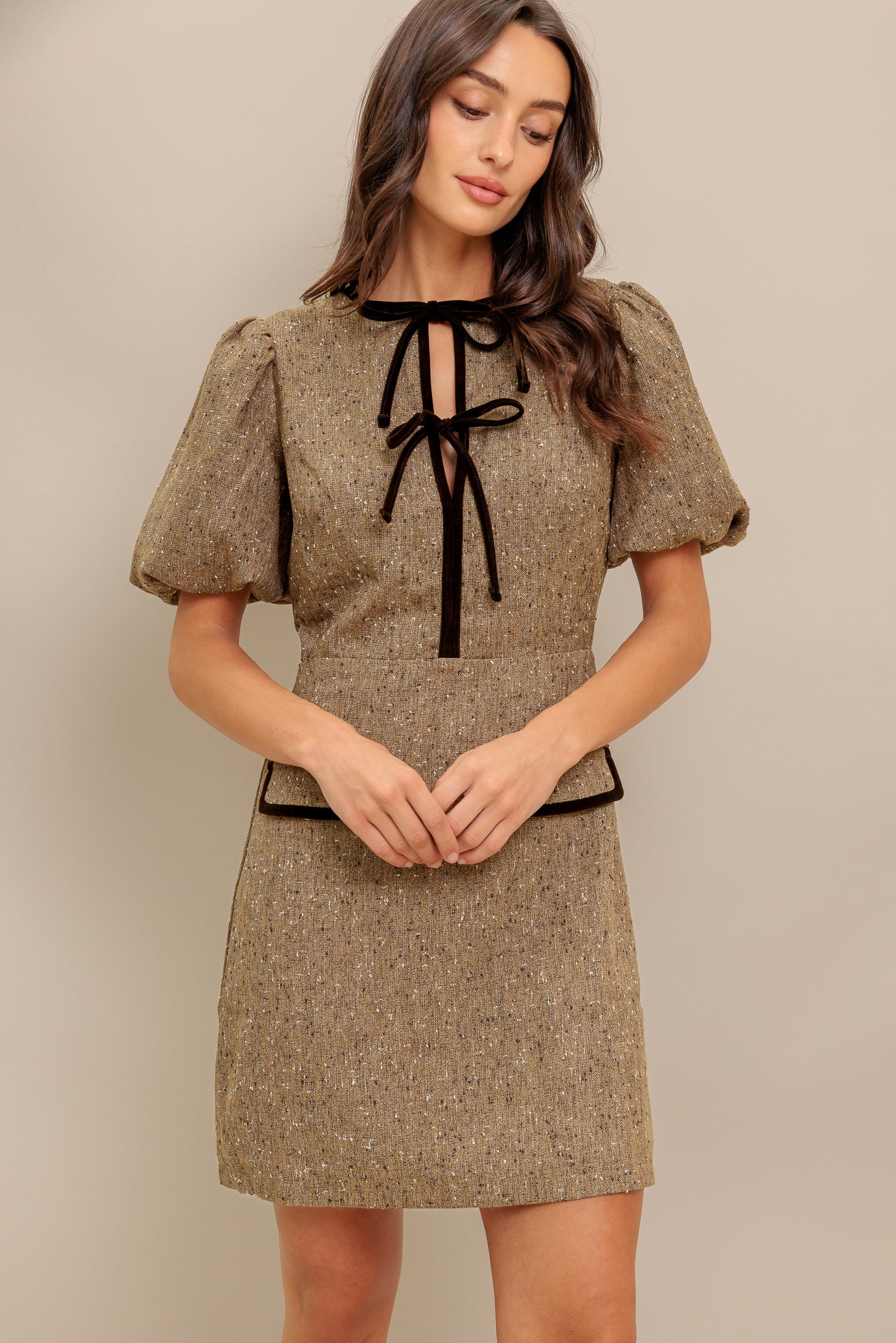 A woven tweed mini dress featuring round neckline, front double bow tie, short puff sleeve, faux pockets and back zipper closure