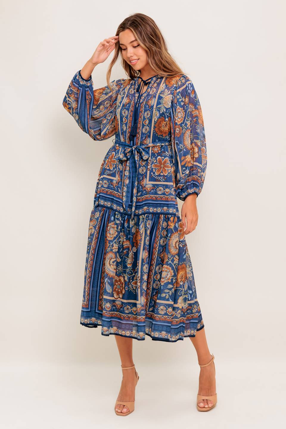 A printed woven midi dress featuring round neckline with front tie, long wide sleeve, self sash tie and ruffled hemline