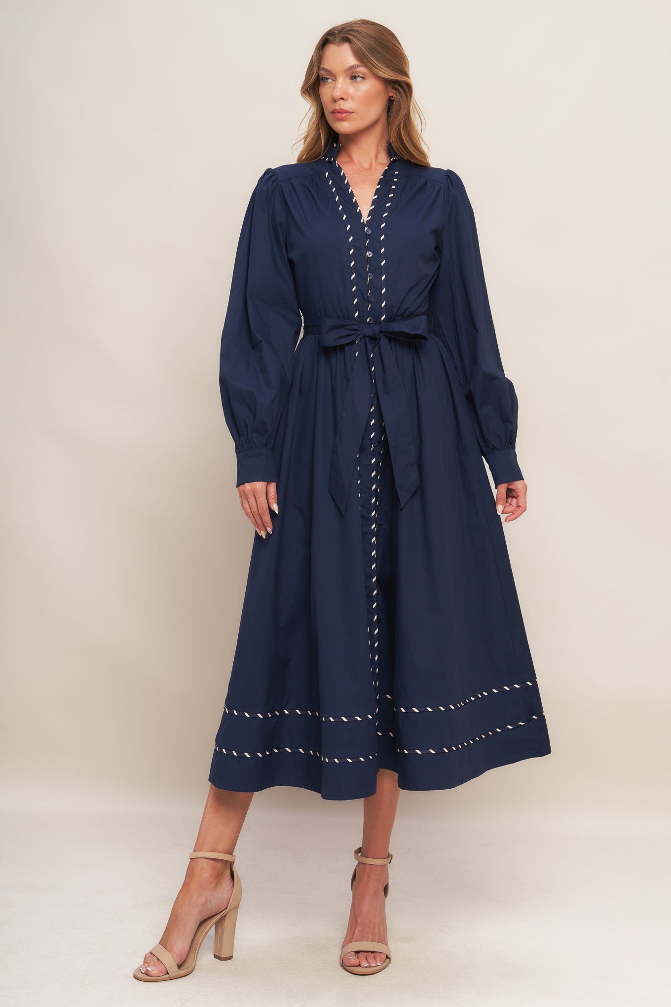 A solid woven midi dress featuring high neckline with V front, long sleeve with cuff, self sash tie, front button down and contrasting binding