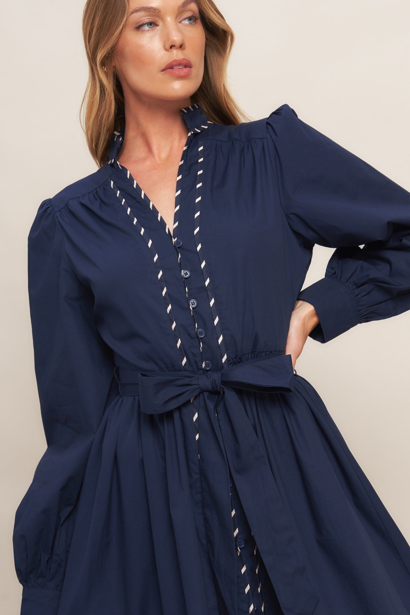 A solid woven midi dress featuring high neckline with V front, long sleeve with cuff, self sash tie, front button down and contrasting binding