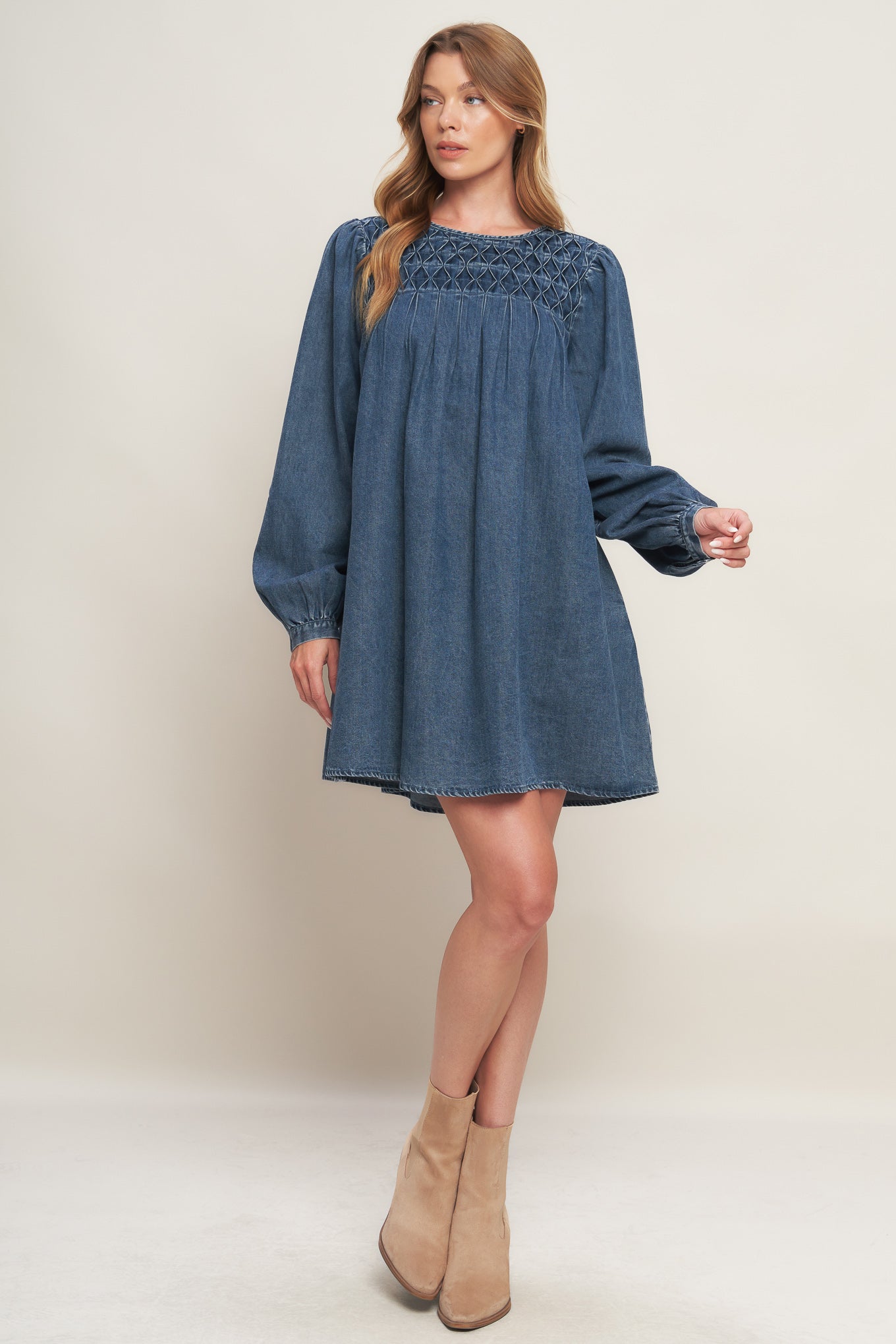 An acid washed mini dress featuring round neckline, honeycomb smocked yoke, long sleeve and back neck button closure