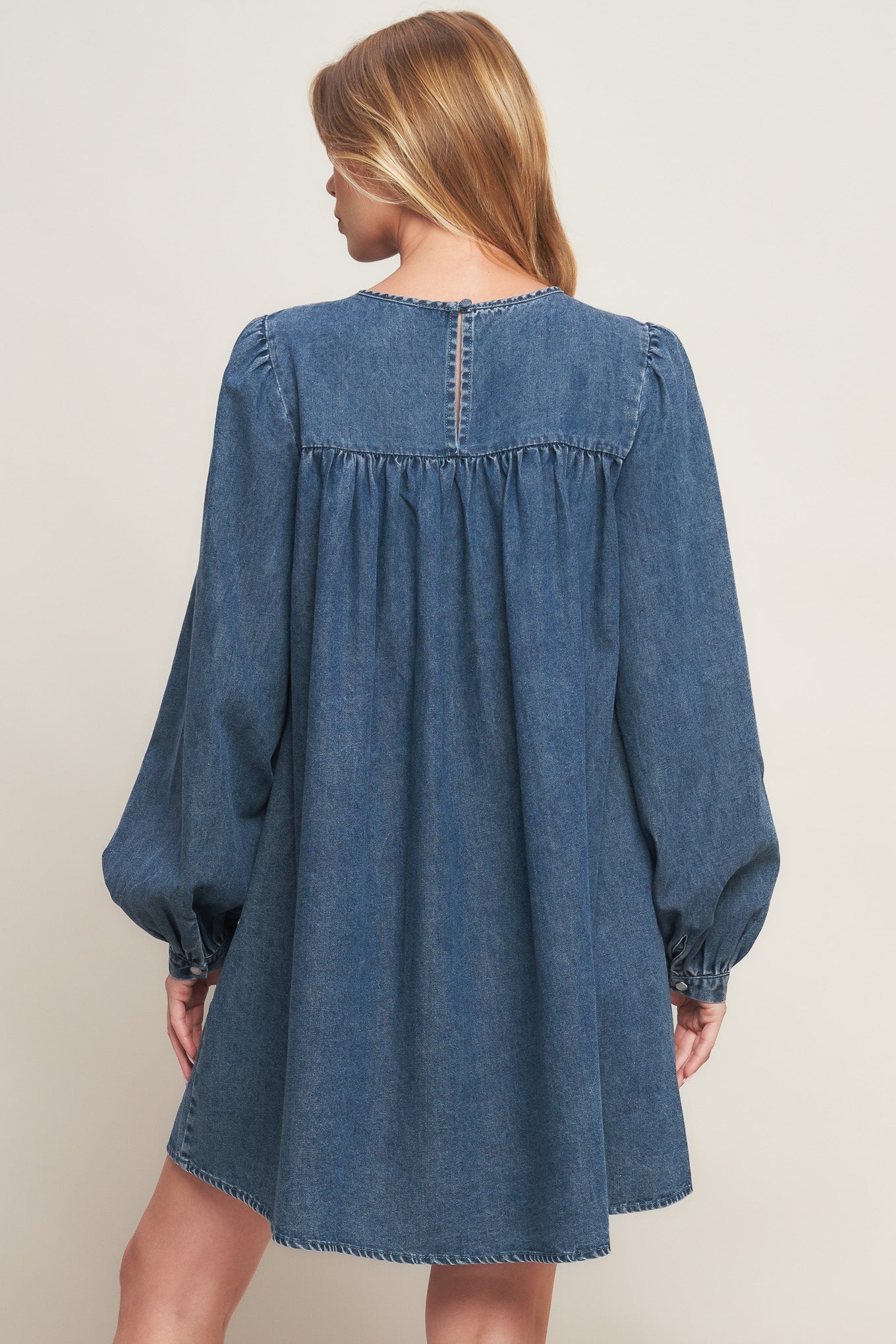An acid washed mini dress featuring round neckline, honeycomb smocked yoke, long sleeve and back neck button closure