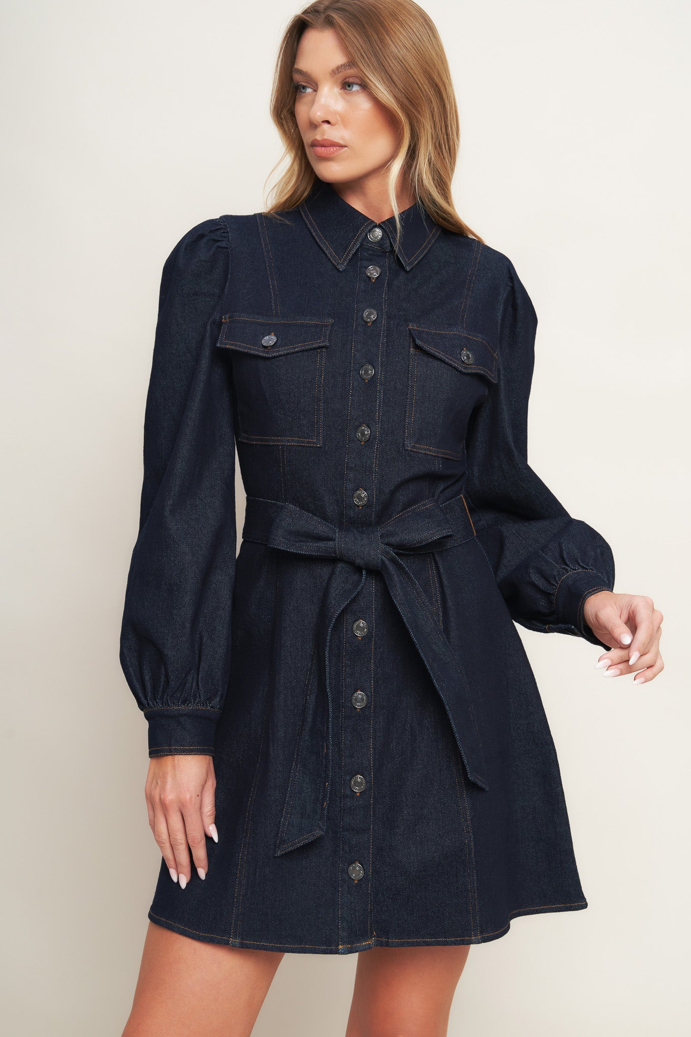 A denim mini dress featuring collar, long sleeve, front pocket, button down closure and self sash tie