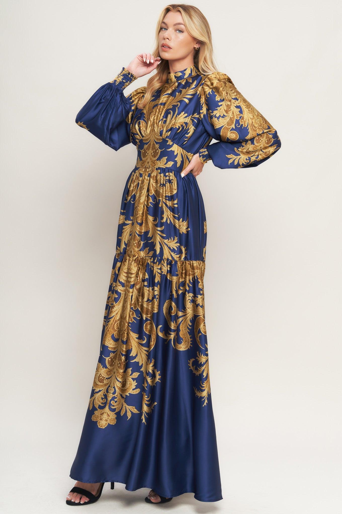 A printed woven maxi dress featuring mock neckline, blouson sleeve with smocked cuff, waist yoke, tiered skirt, smocked back waist band and back neck button closure