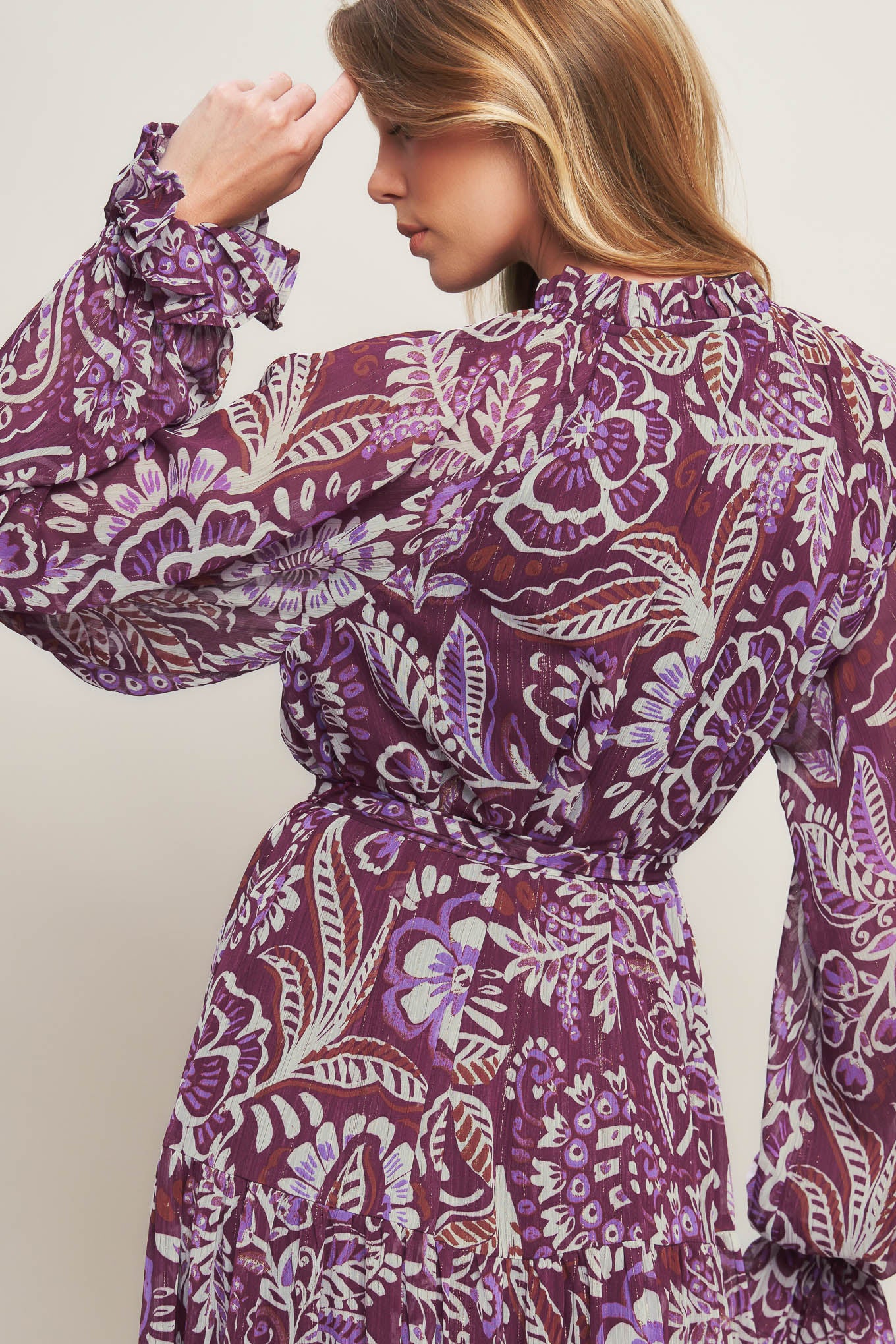 A printed woven maxi dress featuring ruffled neckline with front tie, long sleeve with ruffled cuff, tiered skirt and self sash tie