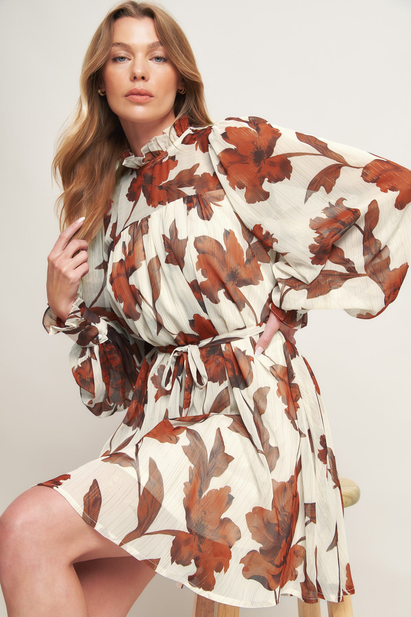 A printed woven mini dress featuring high ruffled neckline, long sleeve with cuff, self sash tie and back neck button closure