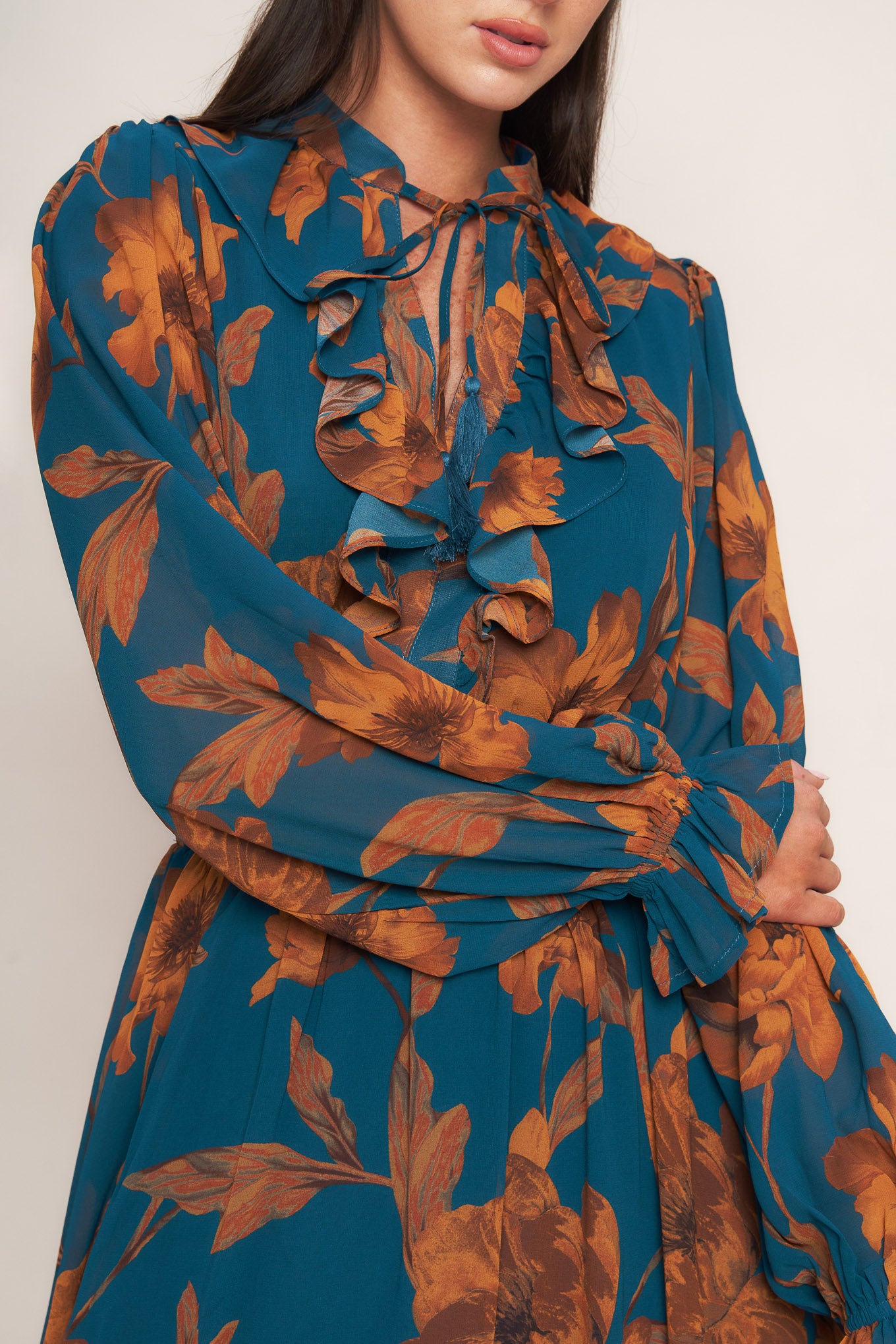 A printed woven midi dress featuring front tie/tassel with ruffles, long sleeve with ruffled cuff and elasticized waist