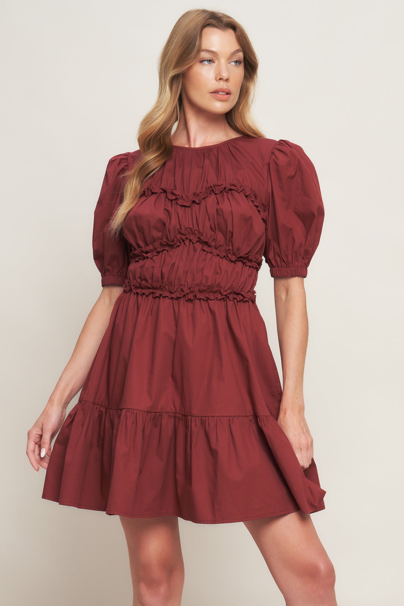 A solid woven mini dress featuring round neckline, short puff sleeve, ruffled hemline and smocked back waist band with button closure