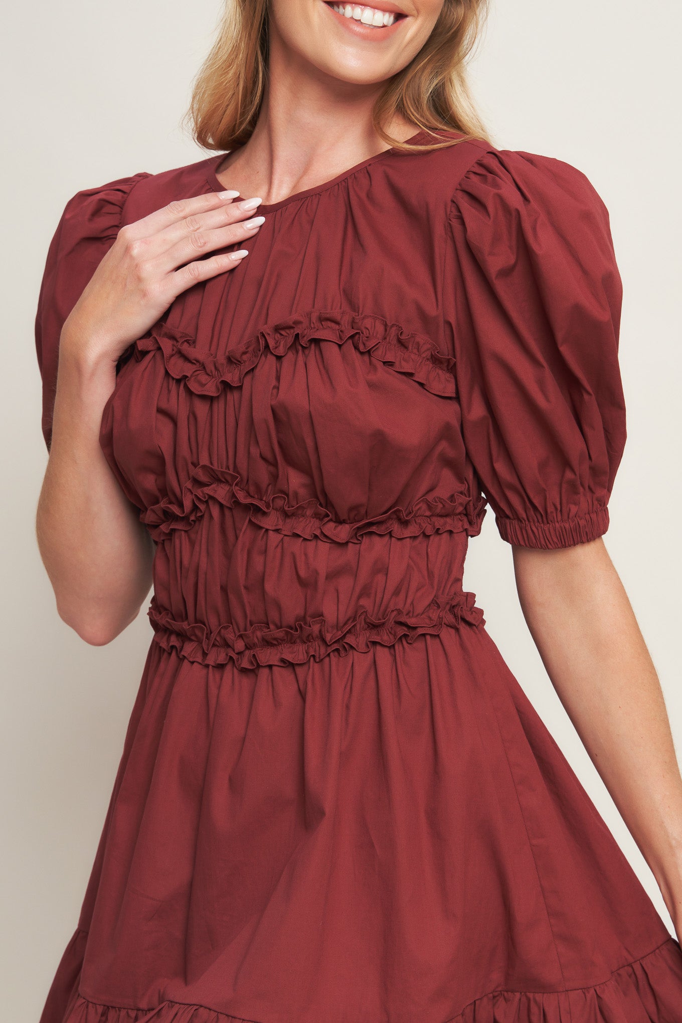 A solid woven mini dress featuring round neckline, short puff sleeve, ruffled hemline and smocked back waist band with button closure