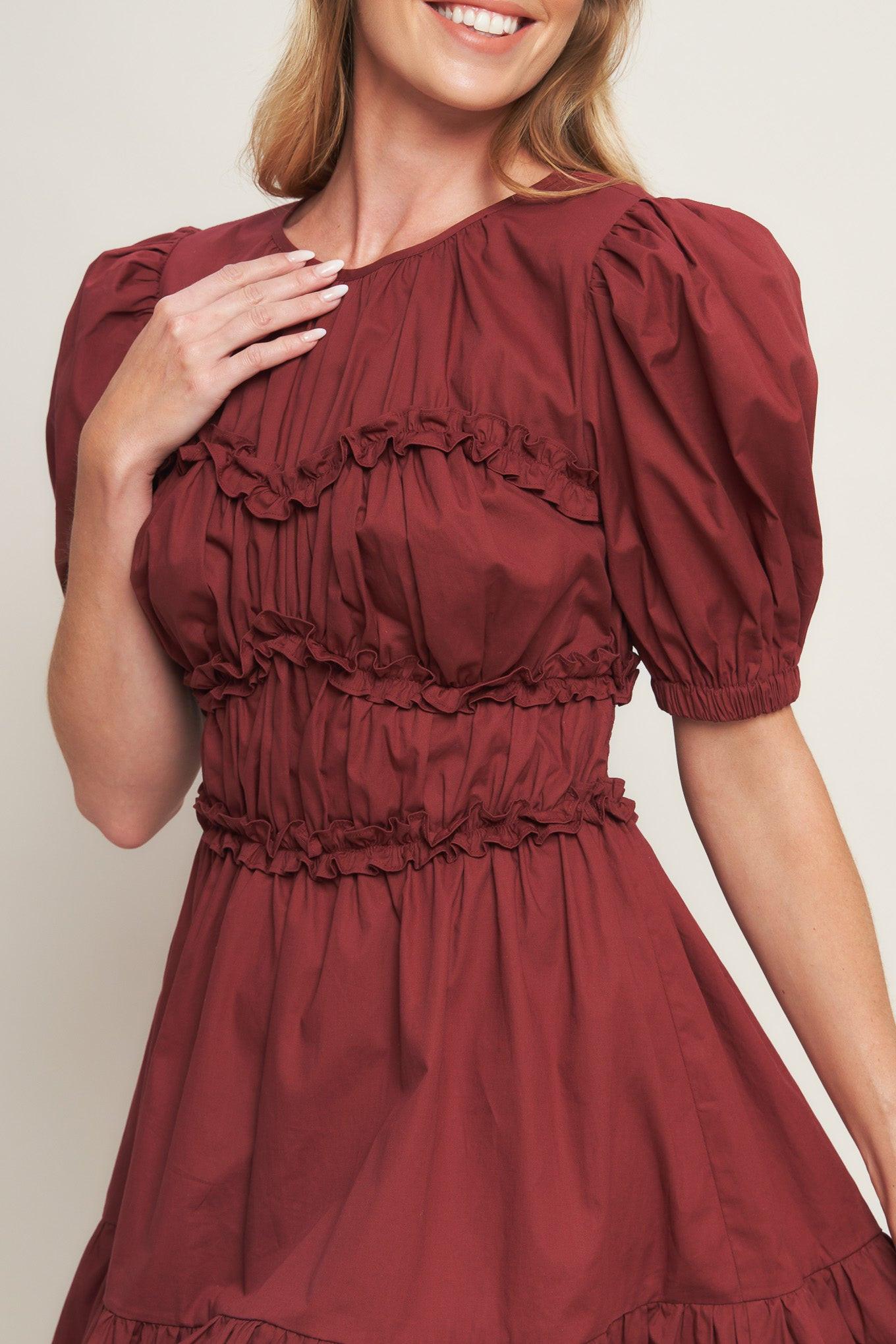 A solid woven mini dress featuring round neckline, short puff sleeve, ruffled hemline and smocked back waist band with button closure