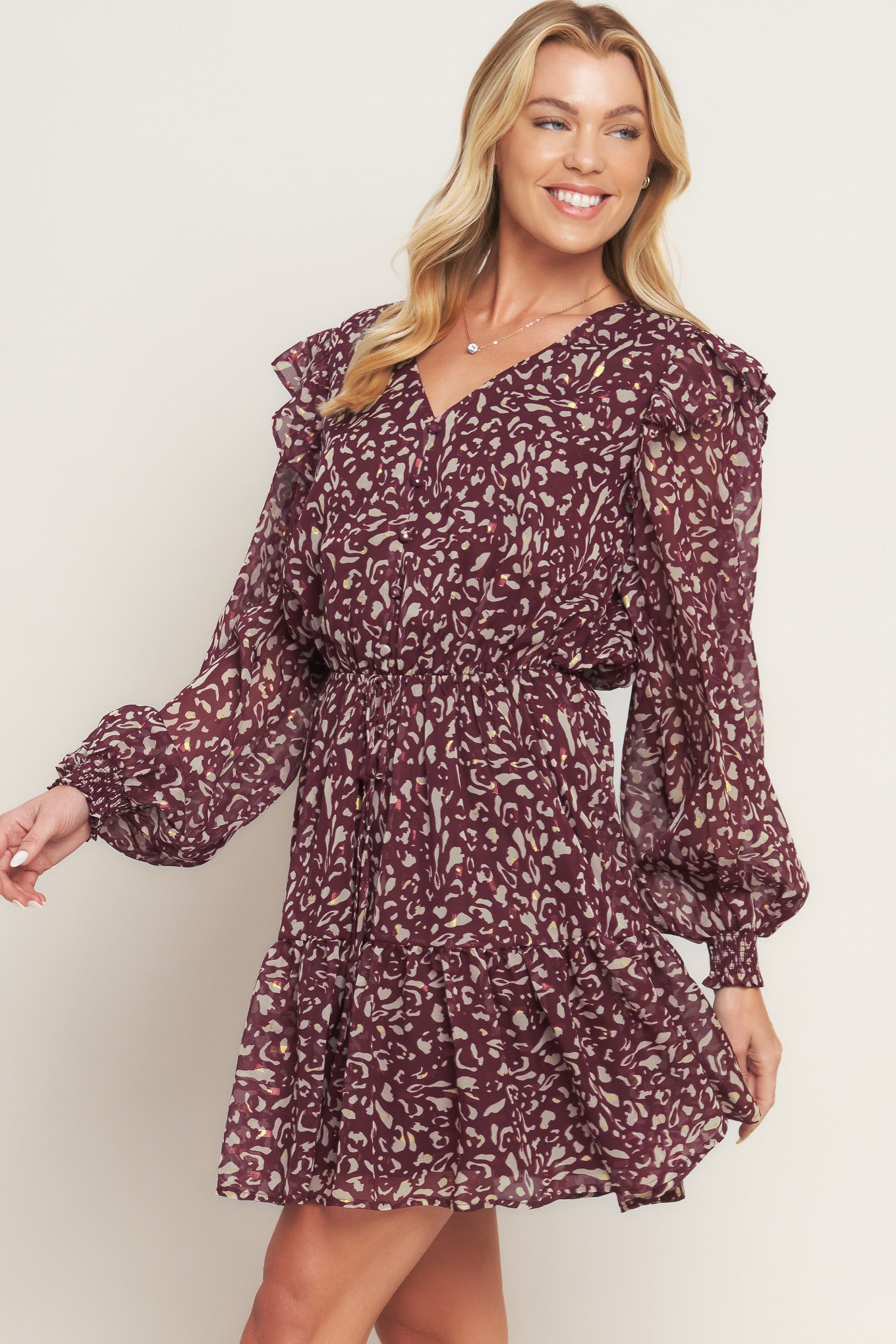 A printed woven mini dress featuring V neckline, long sleeve with ruffled shoulder, front button detail, elasticized waist with front tie and ruffled hemline