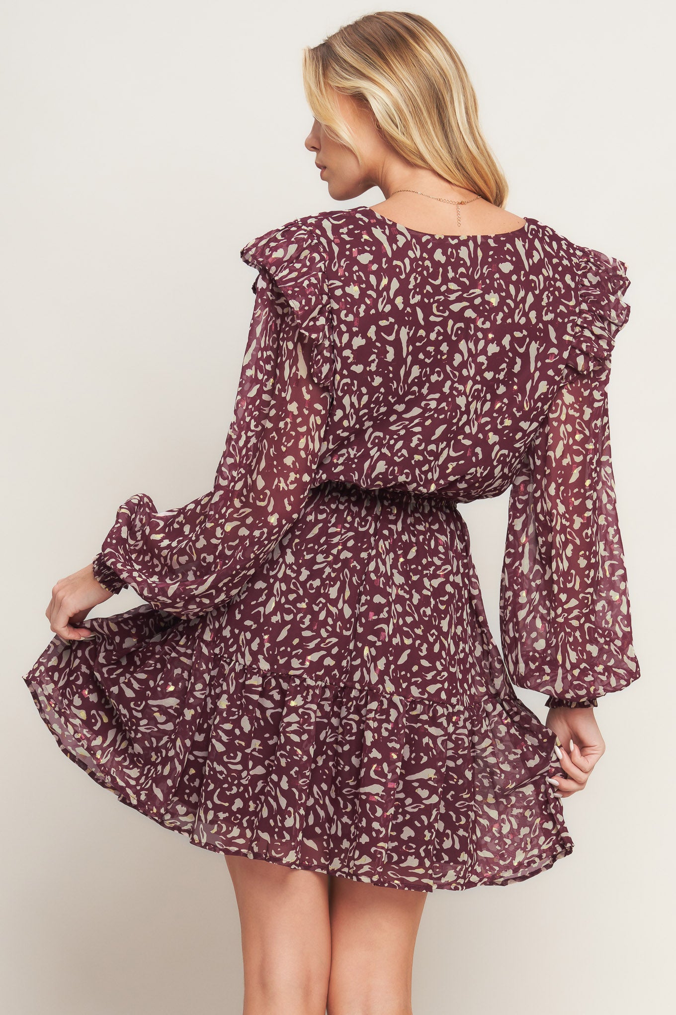 A printed woven mini dress featuring V neckline, long sleeve with ruffled shoulder, front button detail, elasticized waist with front tie and ruffled hemline