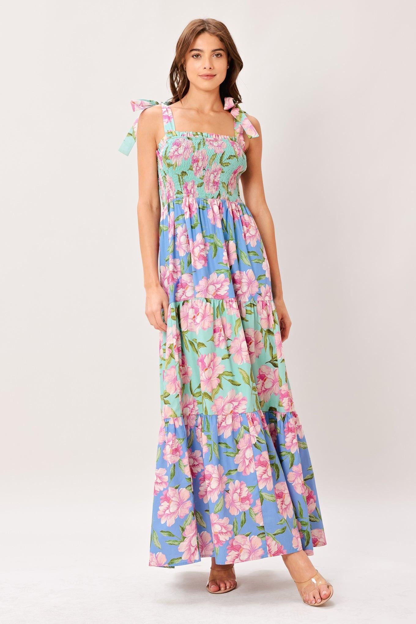 Woman wearing a floral printed woven maxi dress featuring straight neckline with ruffle edge, shoulder tie, smocked bodice and tier skirt