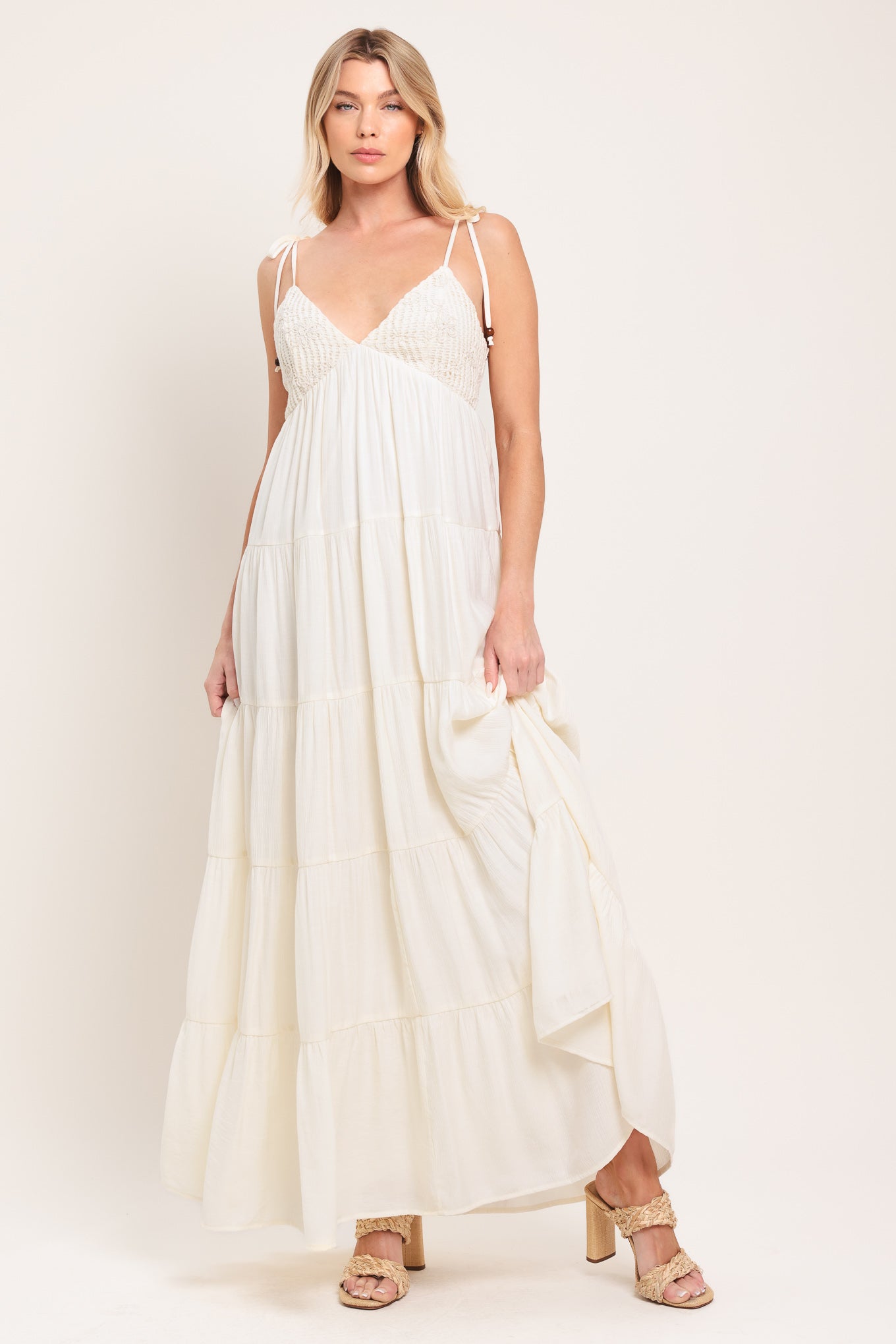Woman wearing a cream flowy maxi dress featuring lace bodice, shoulder tie, tier body and smocked back bodice | Flying Tomato