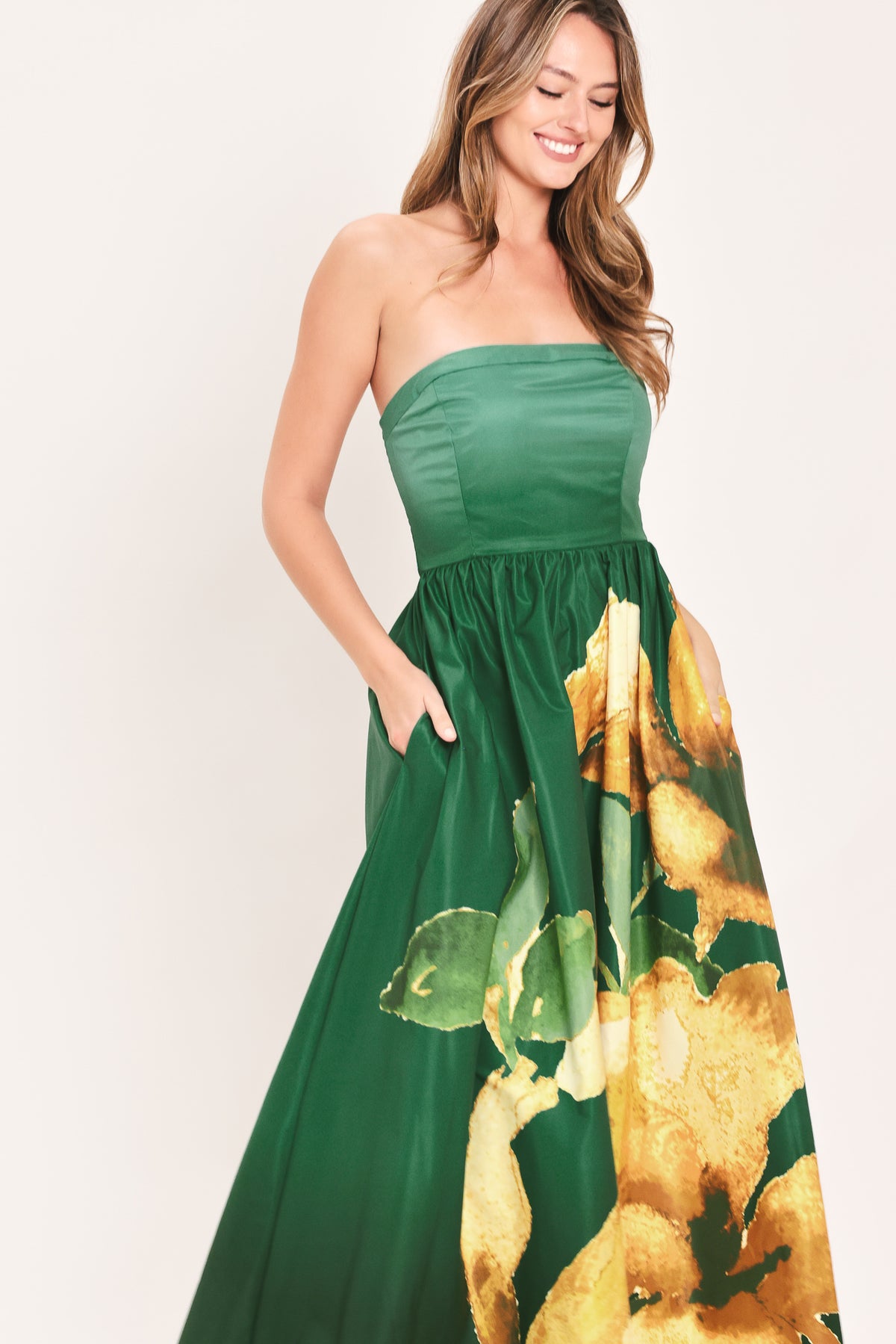 A woman modeling a strapless green maxi dress with a large yellow floral print on the skirt | Flying Tomato