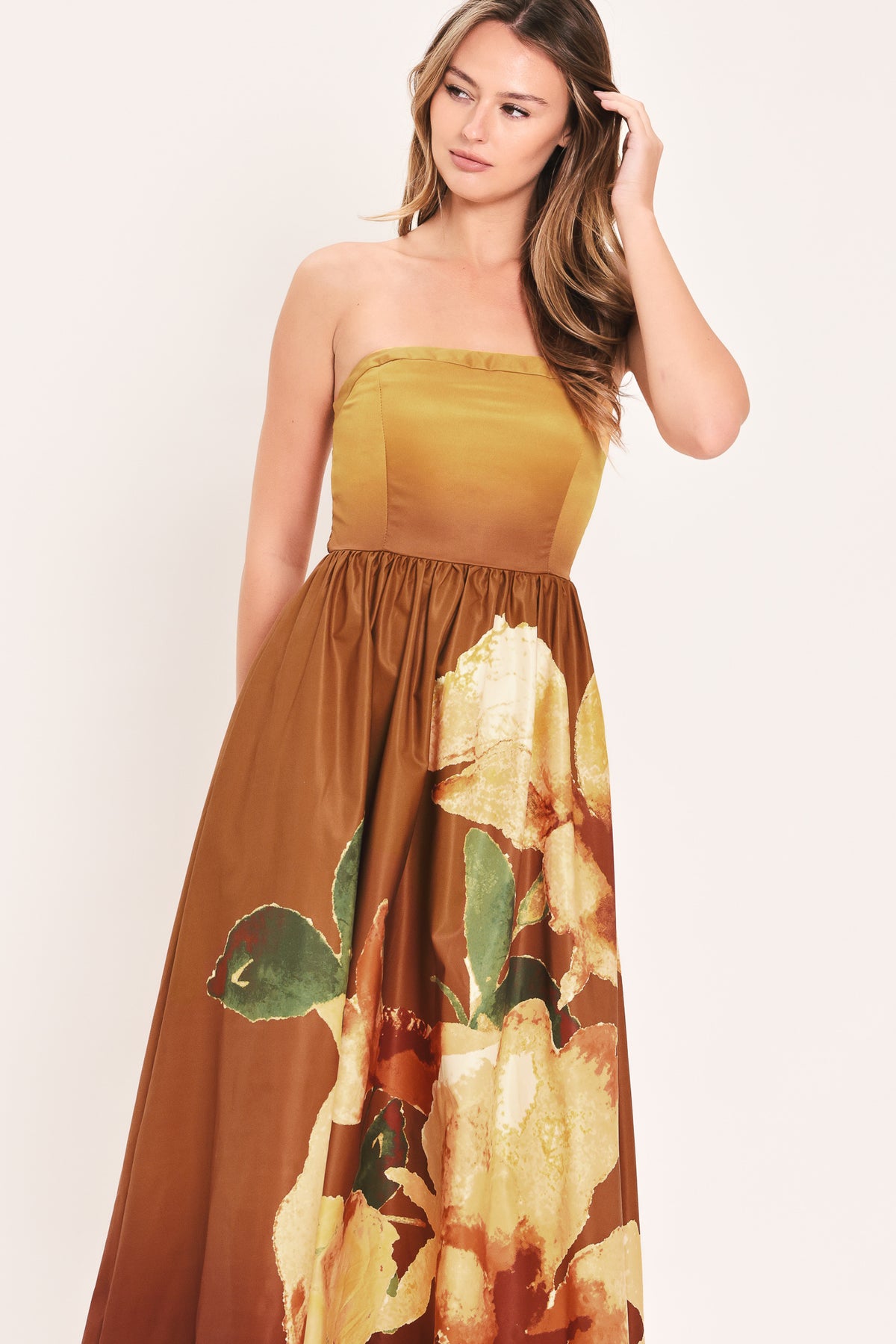 A woman modeling a strapless maxi dress with a mustard yellow bodice and a brown skirt featuring a large yellow floral print with green leaves | Flying Tomato
