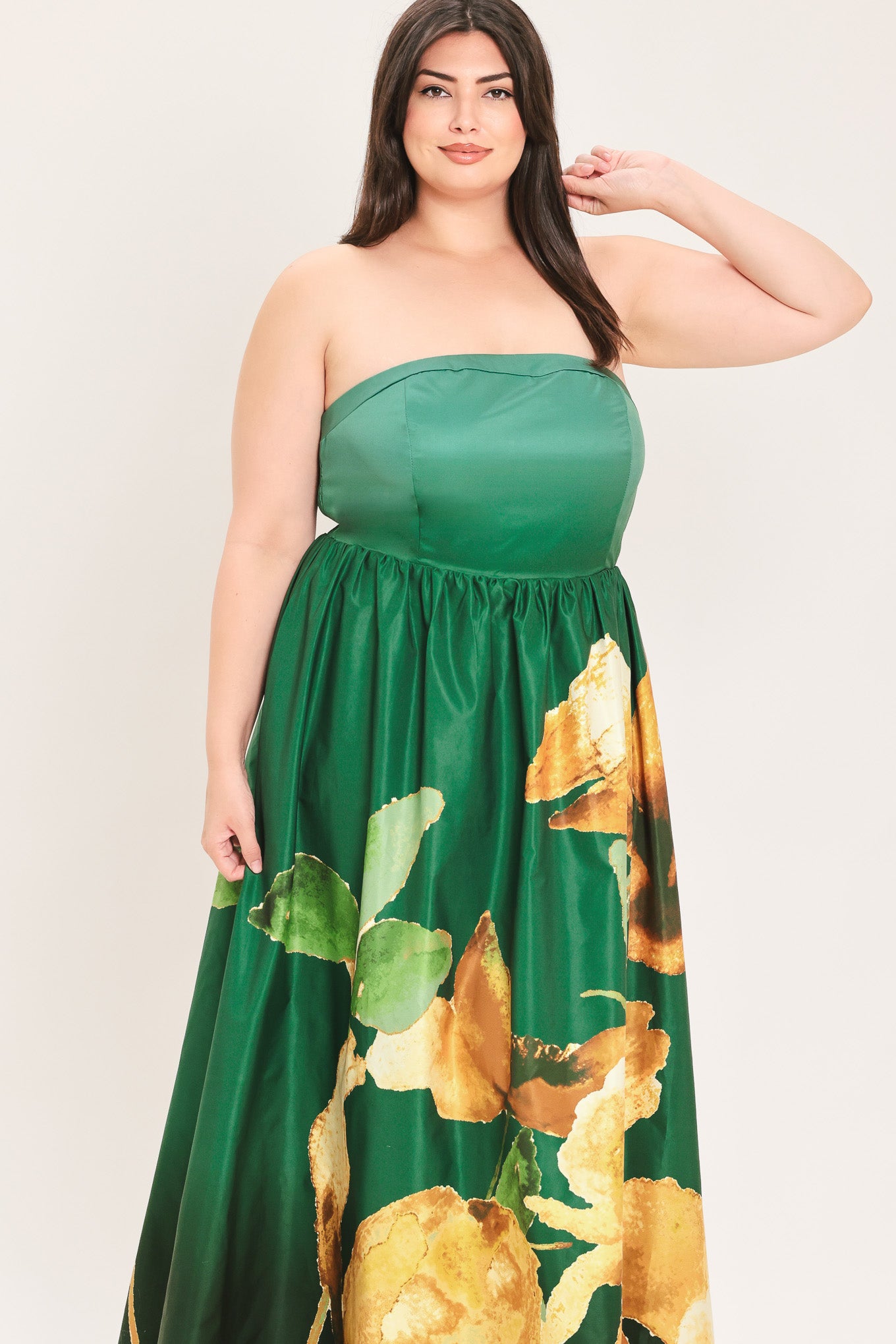 A woman modeling a strapless maxi dress with a green satin-like bodice and a large yellow floral print on a dark green skirt | Flying Tomato Curve