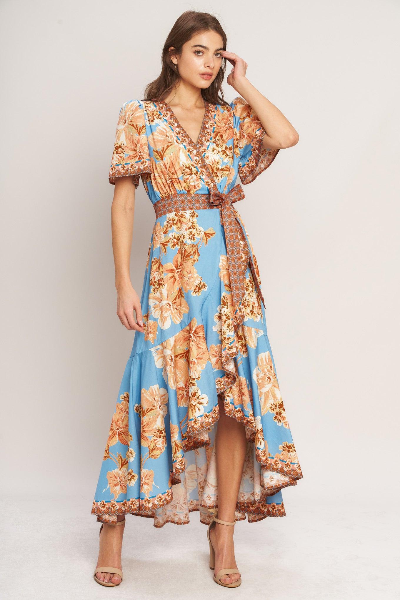 A printed woven hi-lo midi dress featuring surplice neckline, short flutter sleeve, side tie, ruffle hem and smocked back waistband