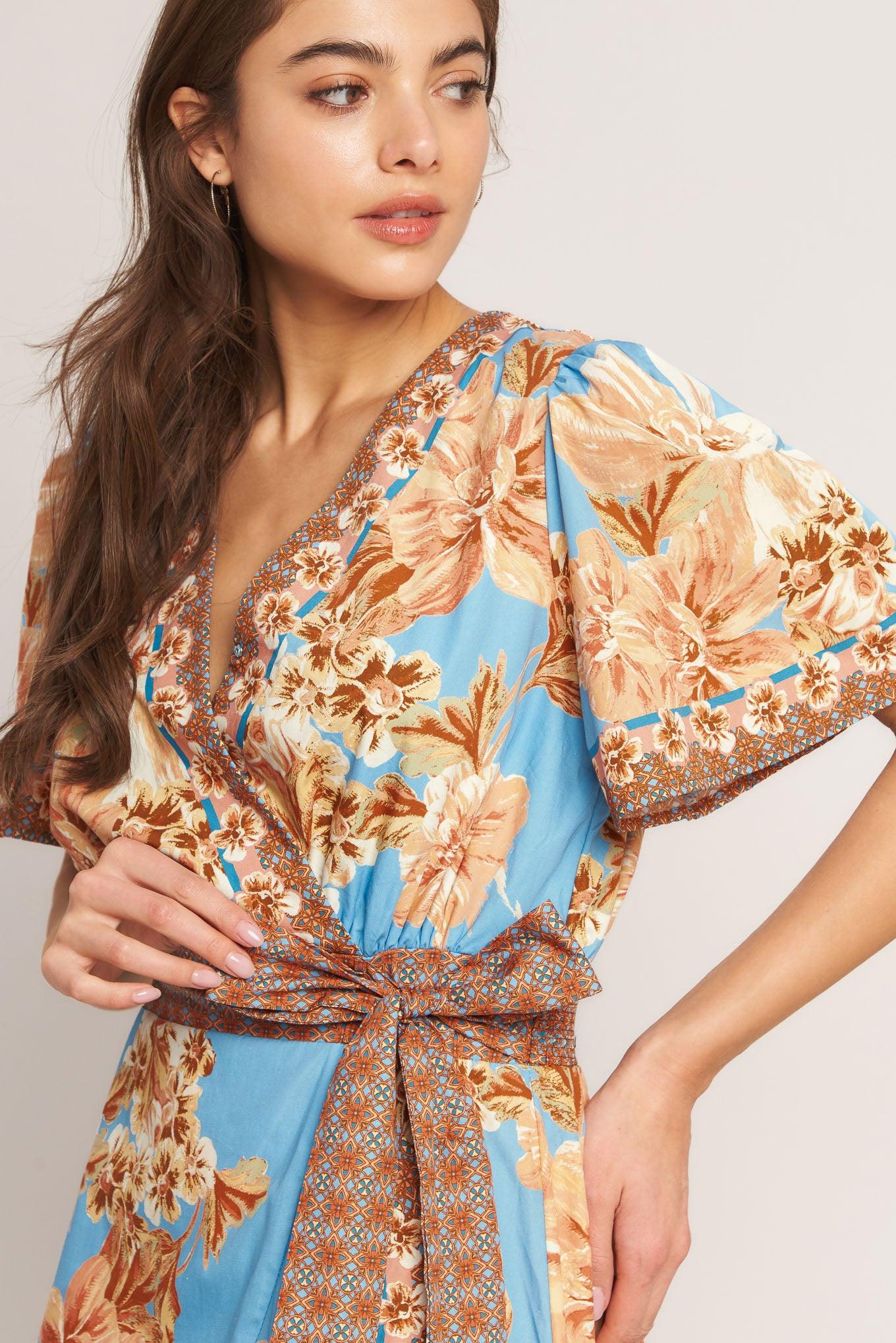 A printed woven hi-lo midi dress featuring surplice neckline, short flutter sleeve, side tie, ruffle hem and smocked back waistband