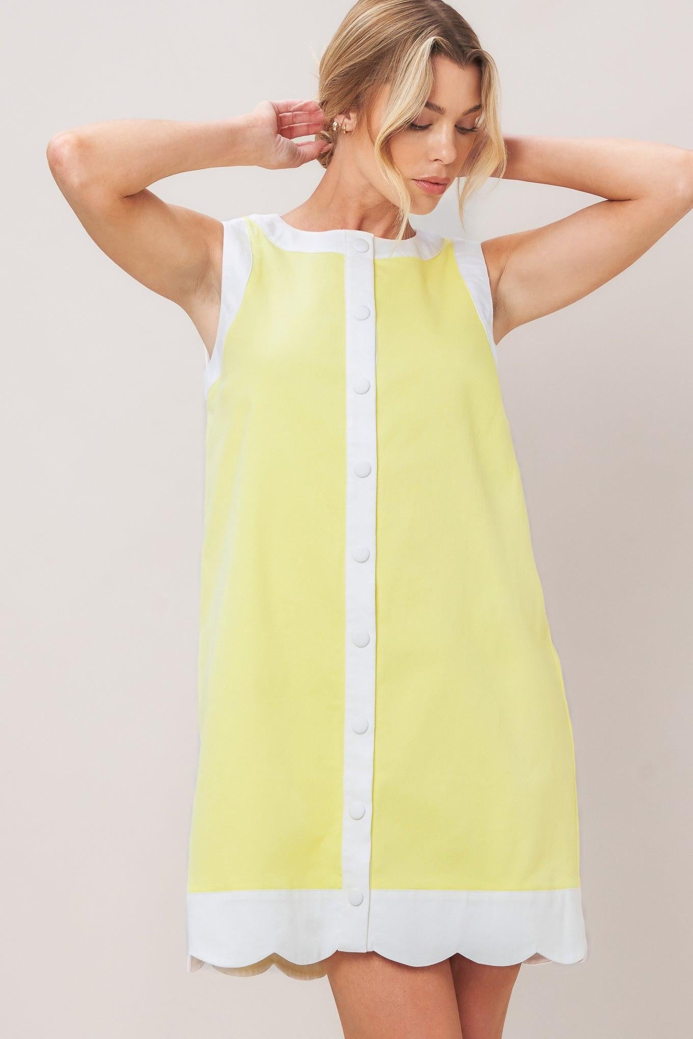 Woman wearing a yellow with white trim mini dress featuring round neckline, sleeveless, front button down and scallop hem