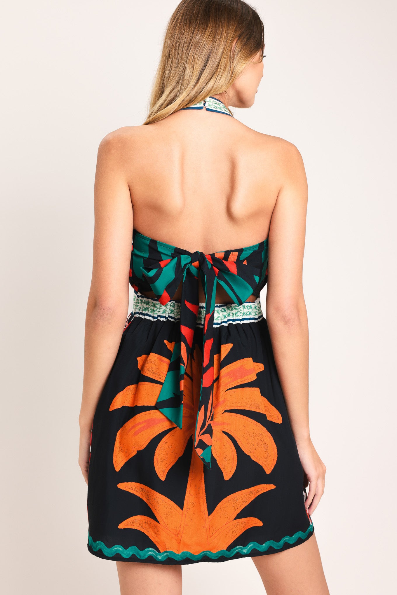 Woman wearing a colorful mini dress with palm tree design featuring twist halter neckline, smocked back waist band and back tie | Flying Tomato