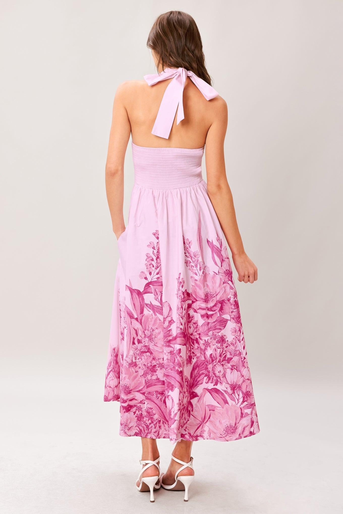 Woman wearing a pink floral printed woven midi dress featuring twist front with back neck tie, full skirt and smocked back bodice
