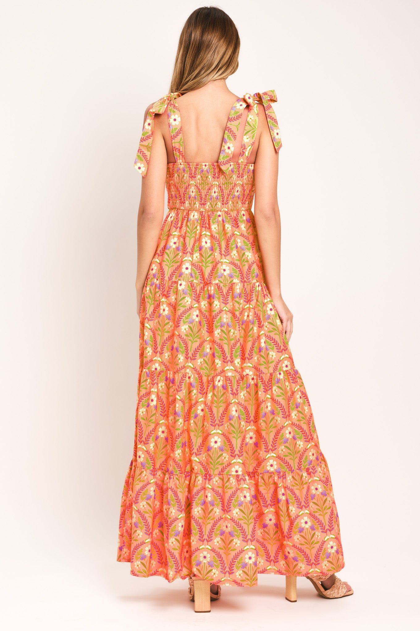 Woman wearing a floral patterned orange maxi dress featuring straight neckline, smocked bodice, shoulder ties and tier skirt | Flying Tomato