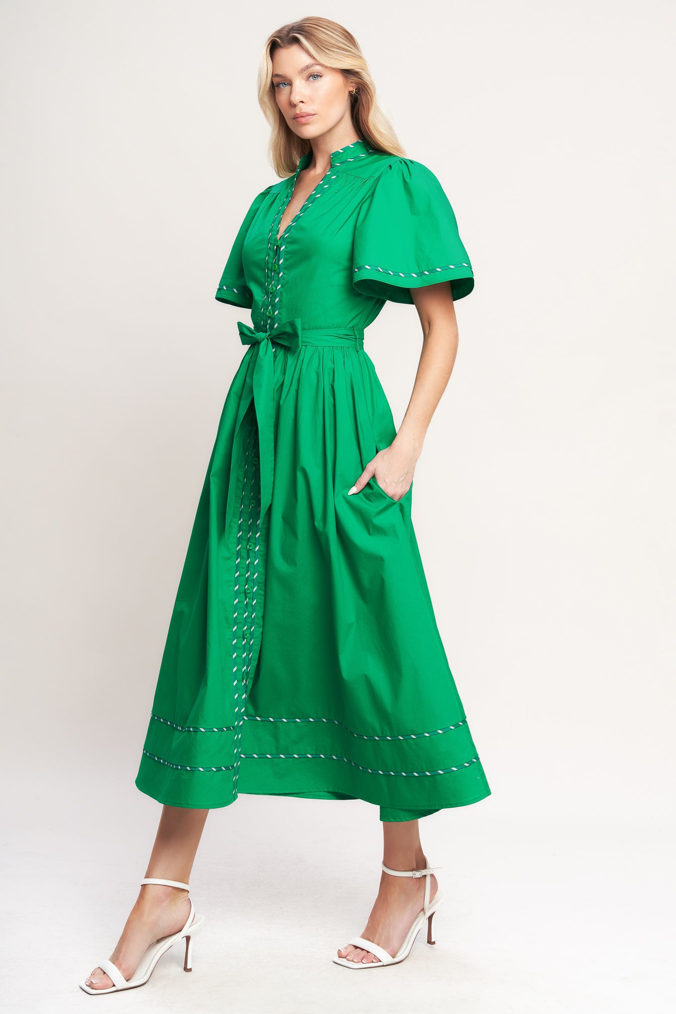 Woman wearing a green midi dress featuring V neckline, short flutter sleeve, button down, self sash tie, contrasting binding and full skirt | Flying Tomato