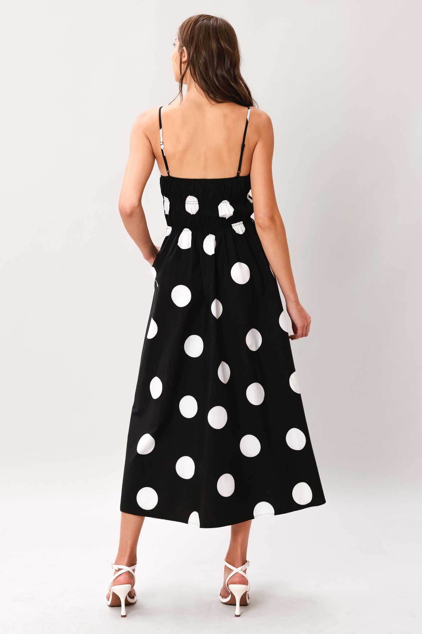 Woman wearing a black midi dress with white polka dots featuring straight neckline, straps, elastic at empire and waist, side pockets and full skirt | Flying Tomato