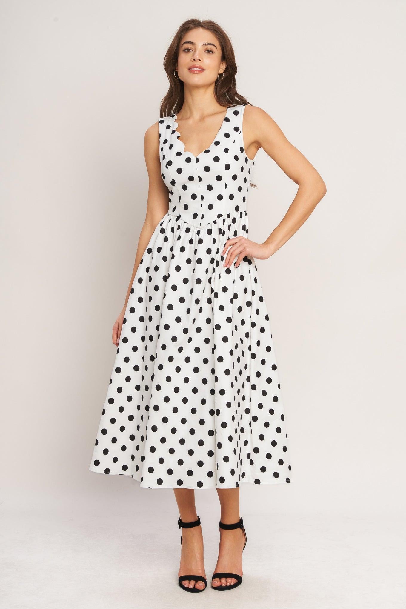 Woman wearing a white dress with black polka dots against a plain background