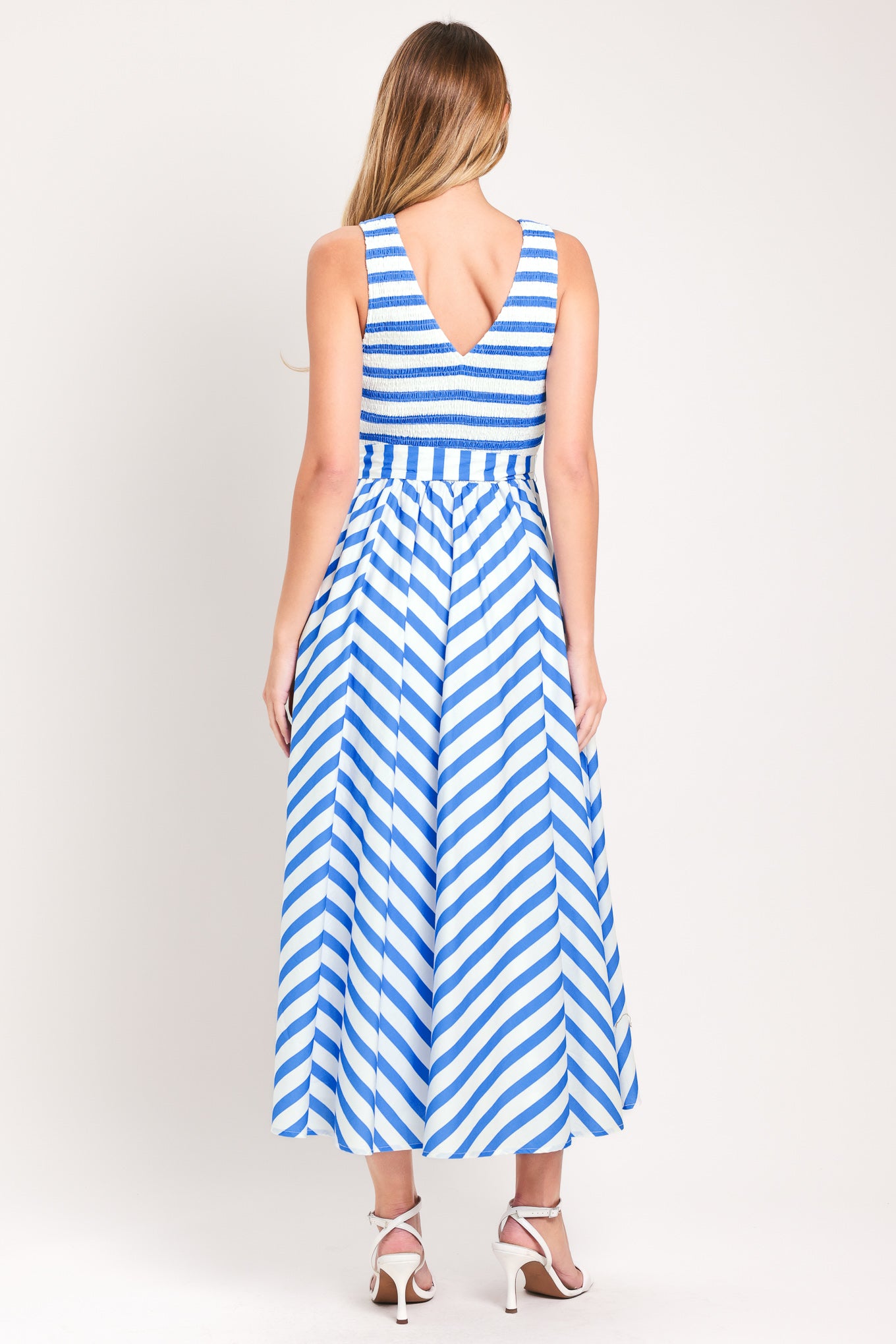 Woman wearing a blue and white striped midi dress featuring V neckline, sleeveless, smocked bodice, self sash tie and full skirt | Flying Tomato