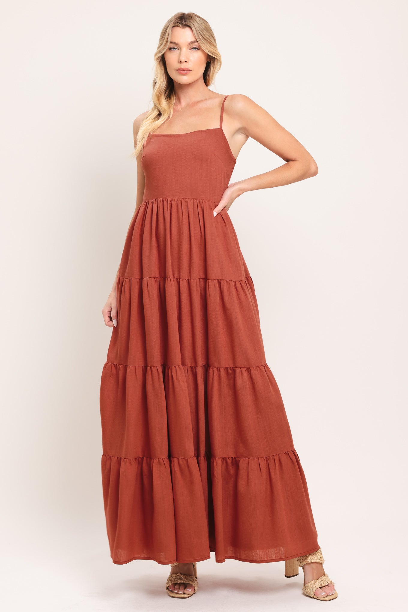 Woman wearing a rust-colored tiered maxi dress featuring cami top, tier skirt and smocked back bodice | Flying Tomato