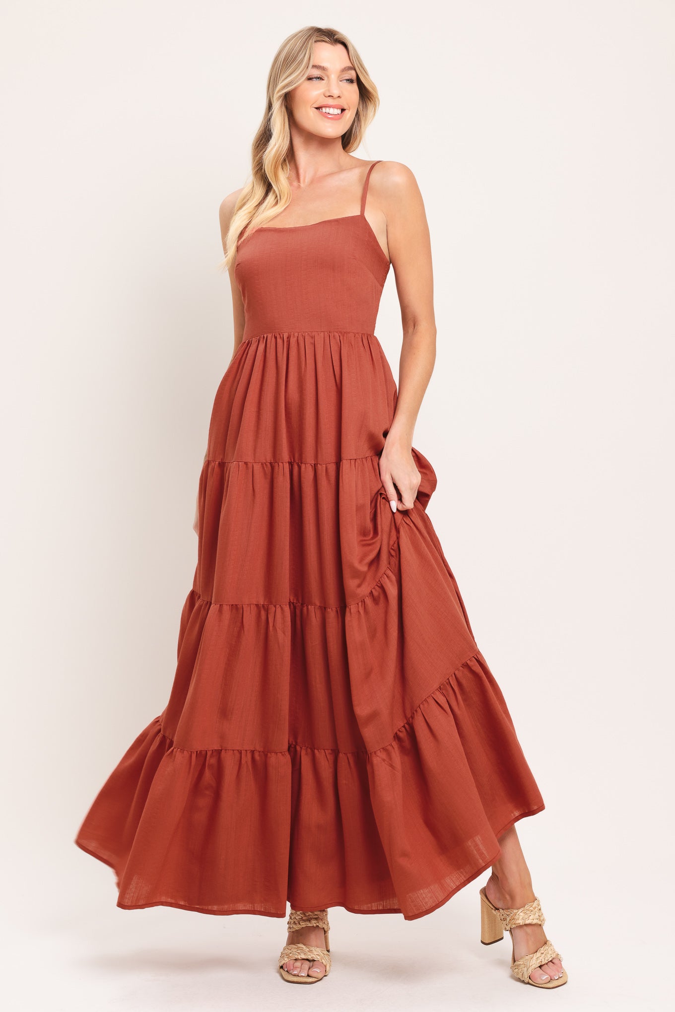 Woman wearing a rust-colored tiered maxi dress featuring cami top, tier skirt and smocked back bodice | Flying Tomato