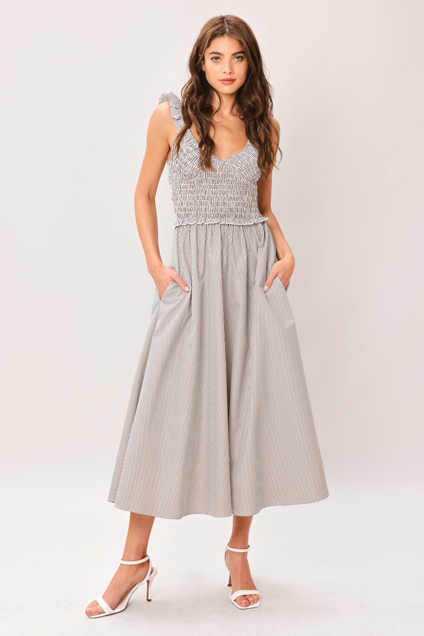 Woman wearing a taupe striped woven midi dress featuring smocked bodice, ruffle strap, side pockets and full skirt | Flying Tomato