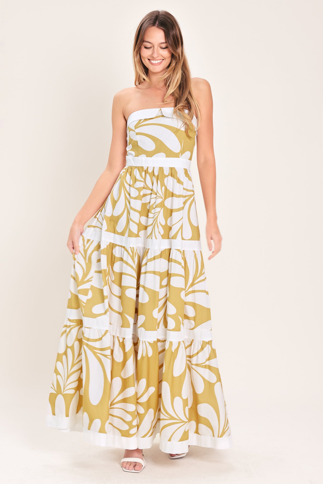 Woman wearing a beige and white maxi dress featuring strapless neckline, tier skirt and back zipper closure | Flying Tomato
