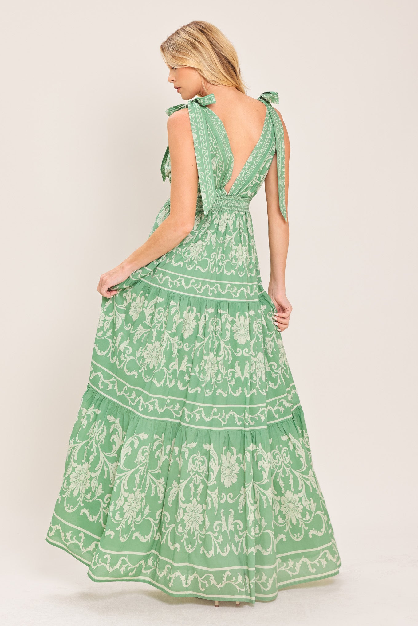 Woman wearing a sage green patterned maxi dress featuring V neckline, shoulder ties, tier skirt and smocked back waistband | Flying Tomato
