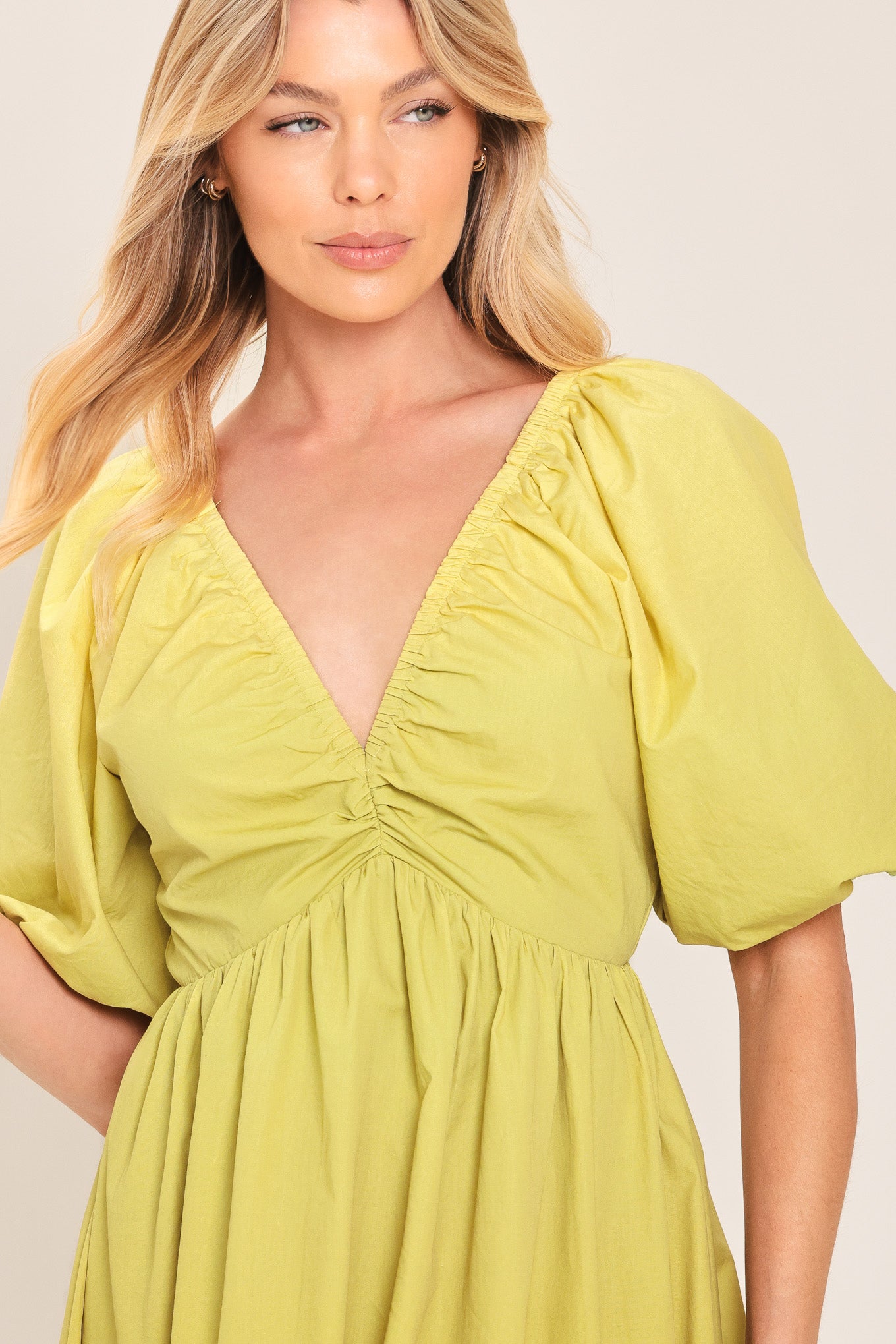 A woman wearing a yellow-green maxi dress with puff sleeves, a gathered V-neckline, and a tiered ruffle hem | Flying Tomato
