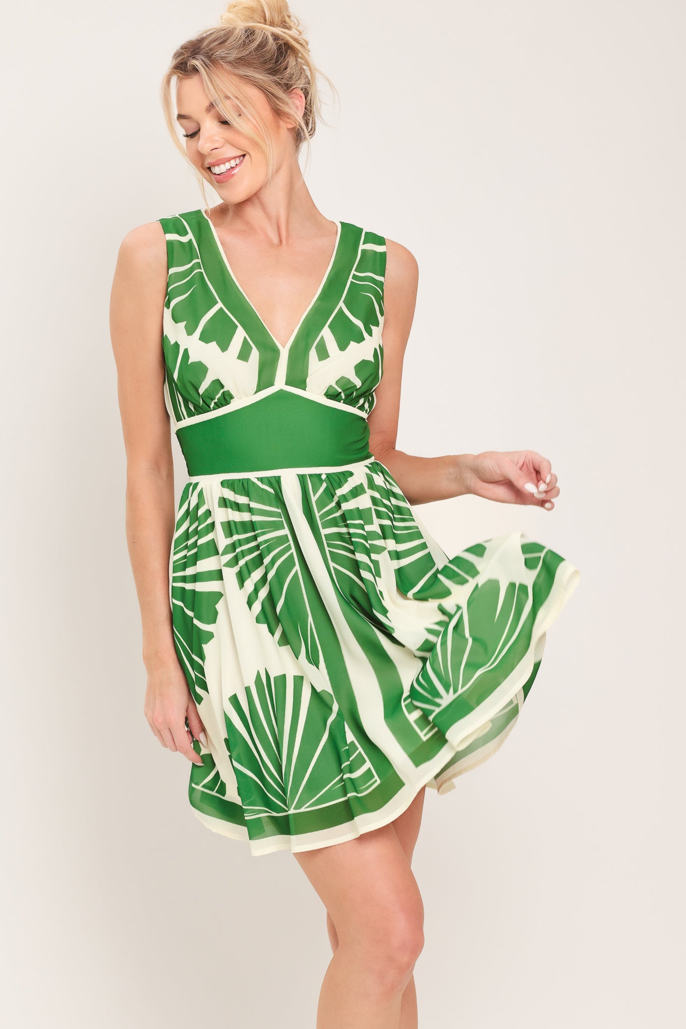 Woman wearing a sleeveless ivory with green leaf pattern mini dress featuring V neckline, full skirt and smocked back waistband | Flying Tomato