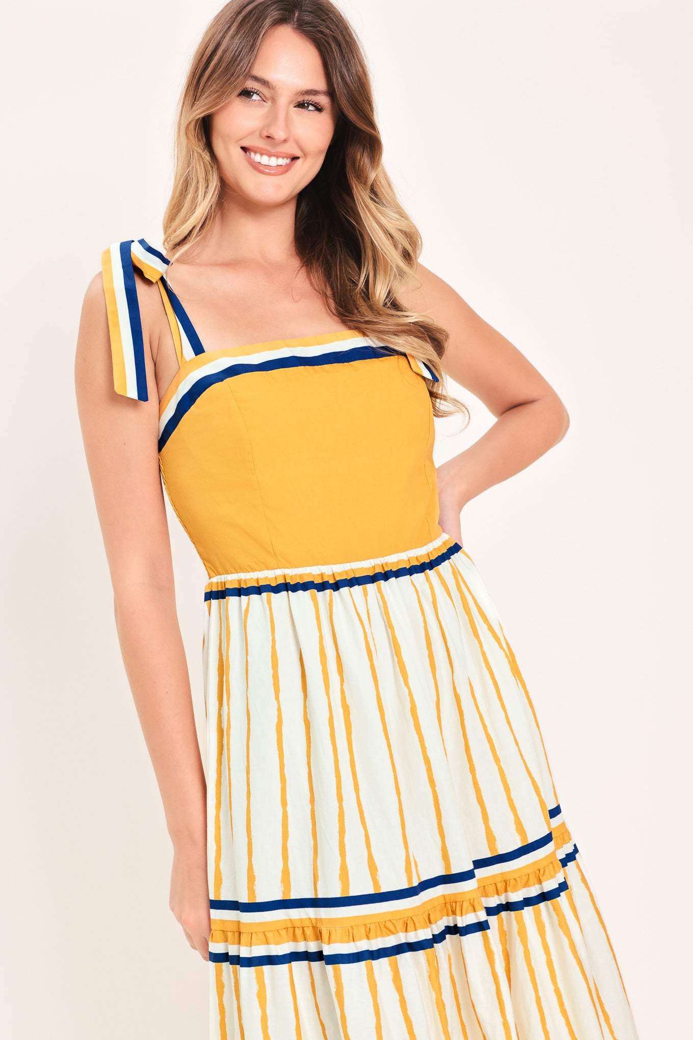Woman wearing a camel yellow and blue striped maxi dress featuring straight neckline, shoulder ties, tier skirt and smocked back bodice | Flying Tomato