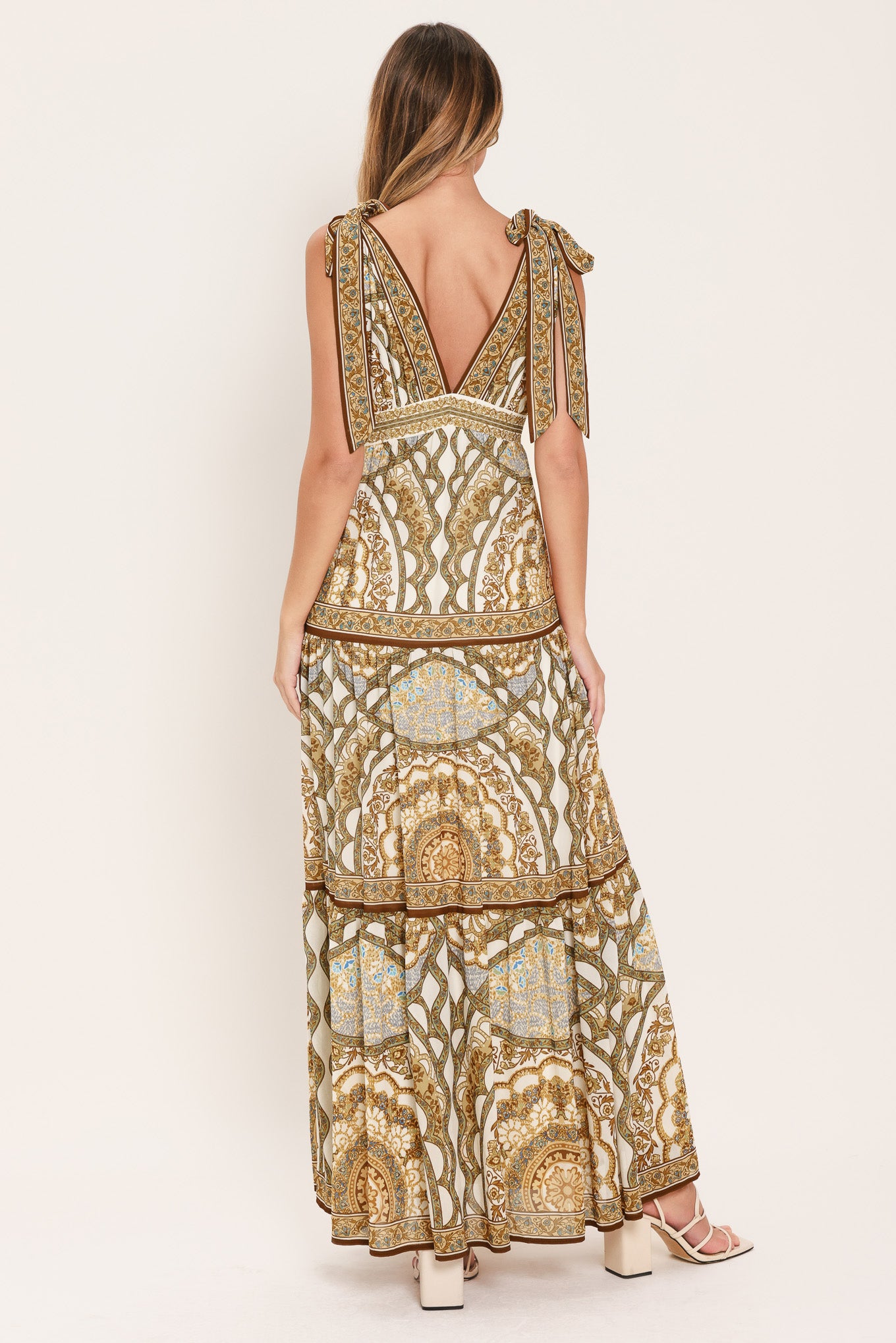 Woman wearing a gold and beige patterned maxi dress featuring front and back V neckline, shoulder ties, smocked waistband and tier skirt | Flying Tomato