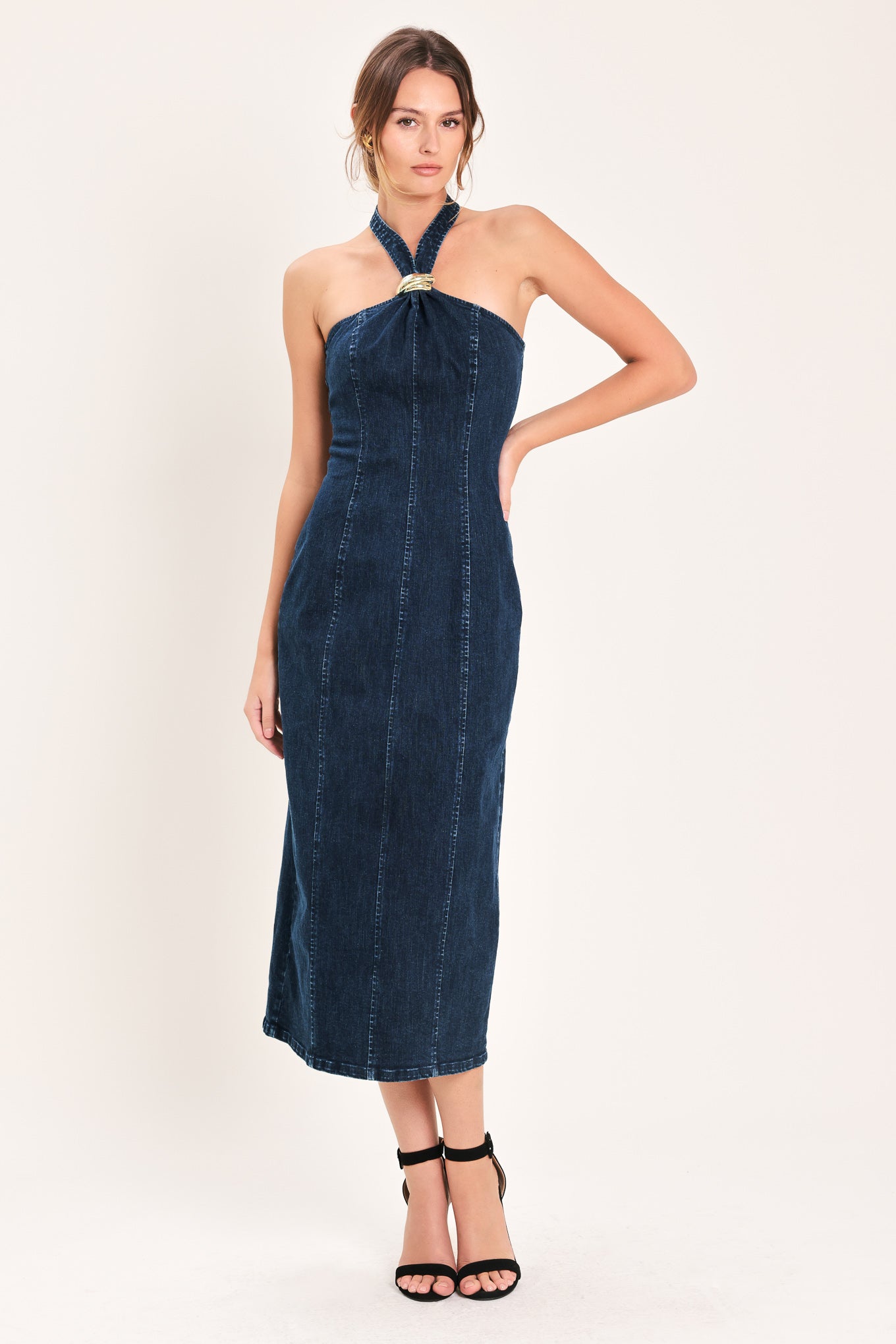 Woman wearing a dark indigo denim midi dress featuring halter neckline with hardware, bare back and zipper closure | Flying Tomato