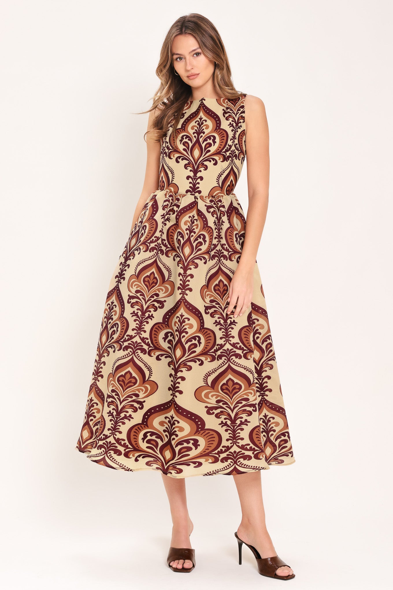 Woman wearing a taupe patterned midi dress featuring round neckline, sleeveless, full skirt and back zipper closure | Flying Tomato