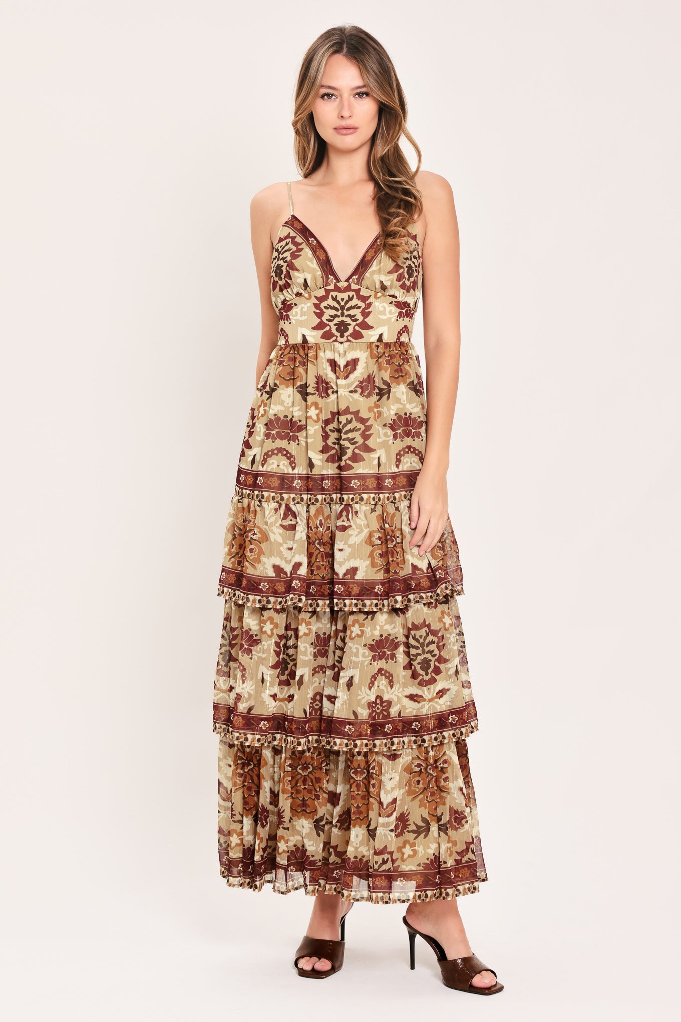 A woman modeling a sleeveless, tiered maxi dress with a bohemian-style floral and geometric pattern in brown and beige | Flying Tomato