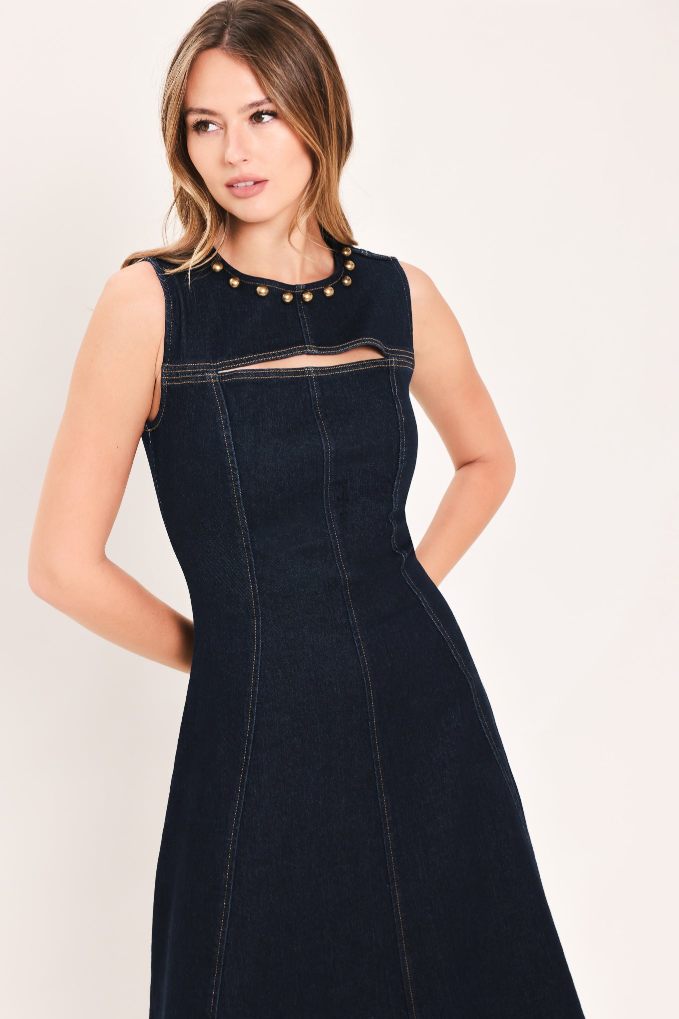 A woman wearing a sleeveless dark navy maxi dress with a crew neckline, a horizontal cutout across the chest, and small gold stud embellishments | Flying Tomato