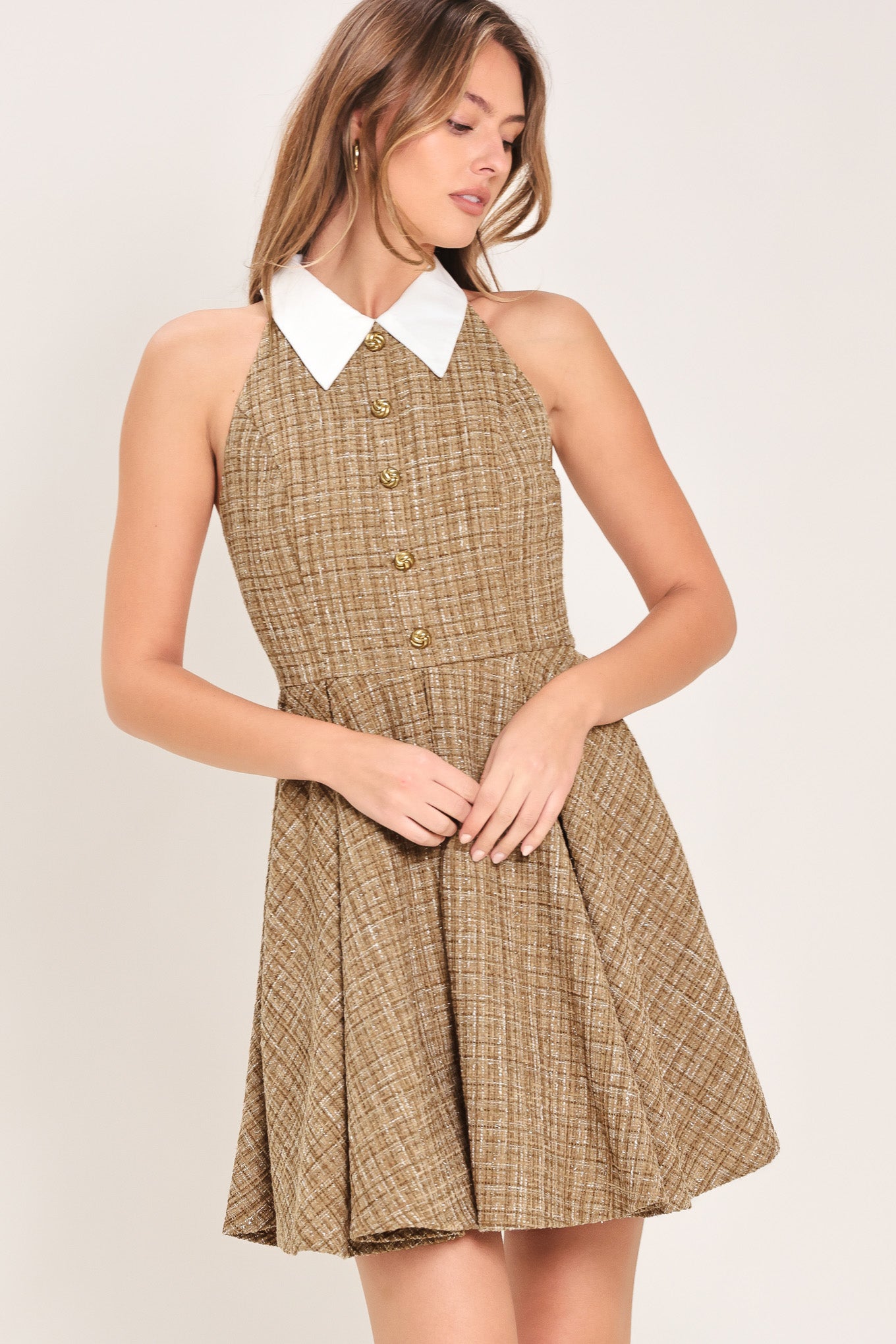 Woman wearing a hazel tweed mini dress featuring halter neckline with white collar finish, front button detail, full circle skirt and back zipper closure background | Flying Tomato