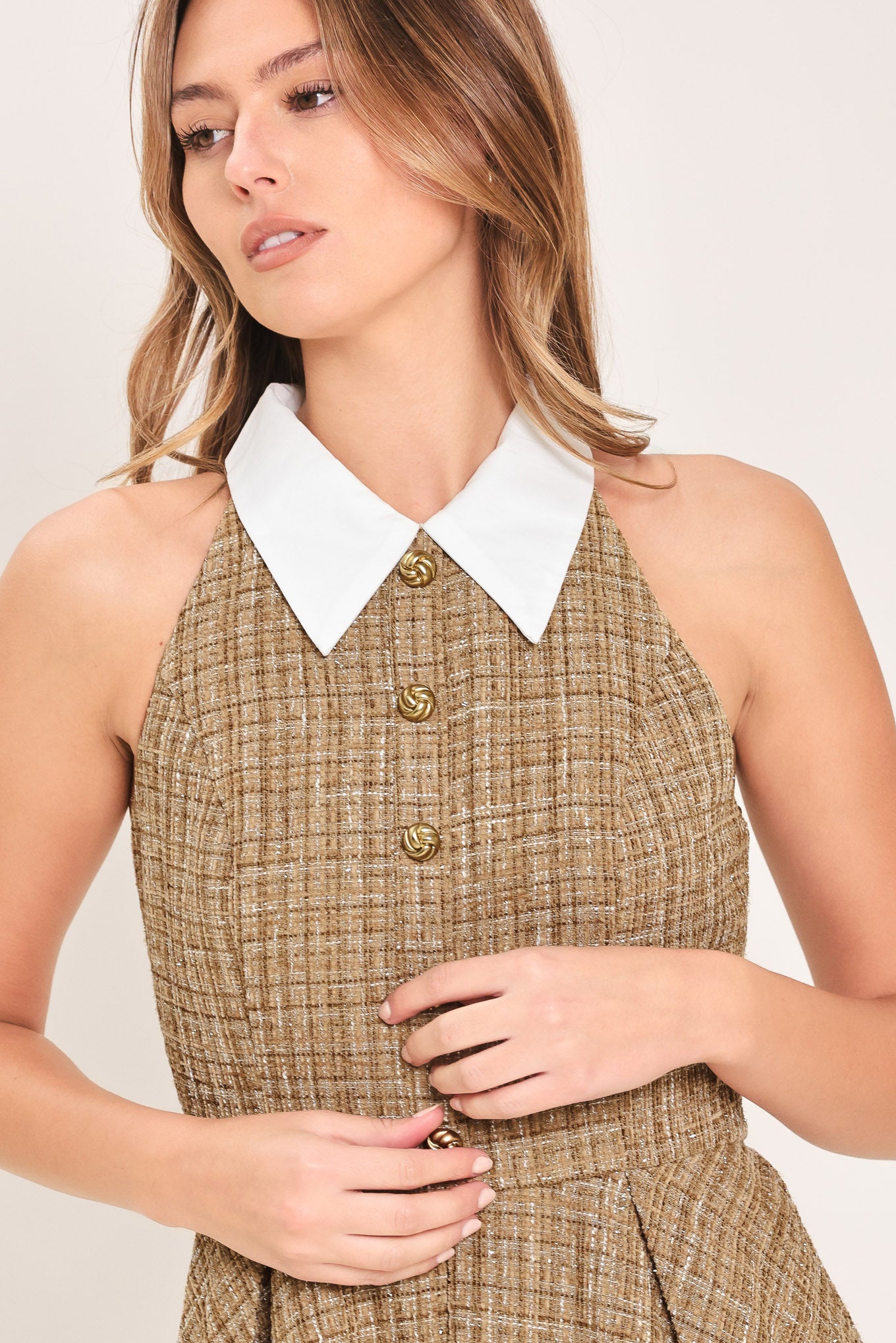 Woman wearing a hazel tweed mini dress featuring halter neckline with white collar finish, front button detail, full circle skirt and back zipper closure background | Flying Tomato