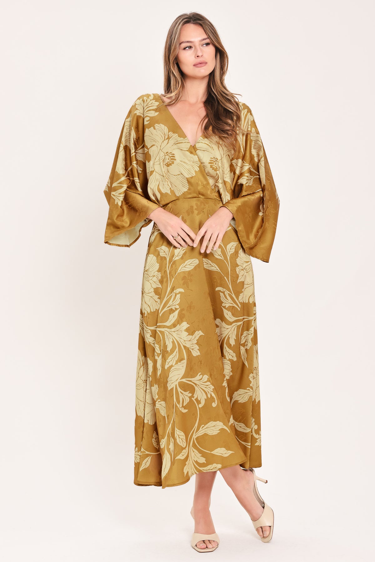 A woman wearing a midi-length, V-neck dress with wide bell sleeves in a golden camel fabric featuring a cream floral jacquard pattern | Flying Tomato