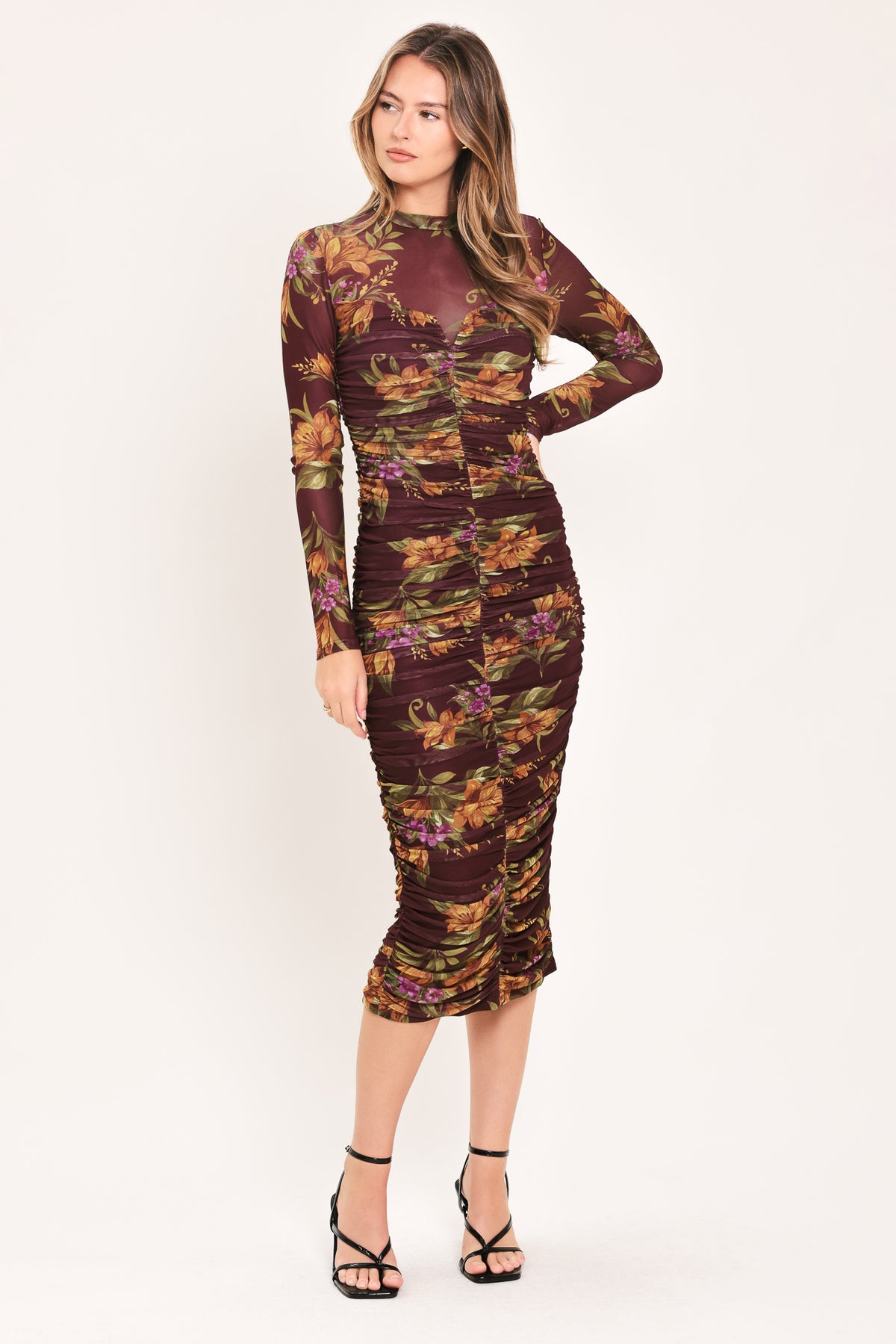 A woman modeling a long-sleeve ruched midi dress with a dark burgundy base and an autumn leaf pattern in orange, yellow, and green | Flying Tomato