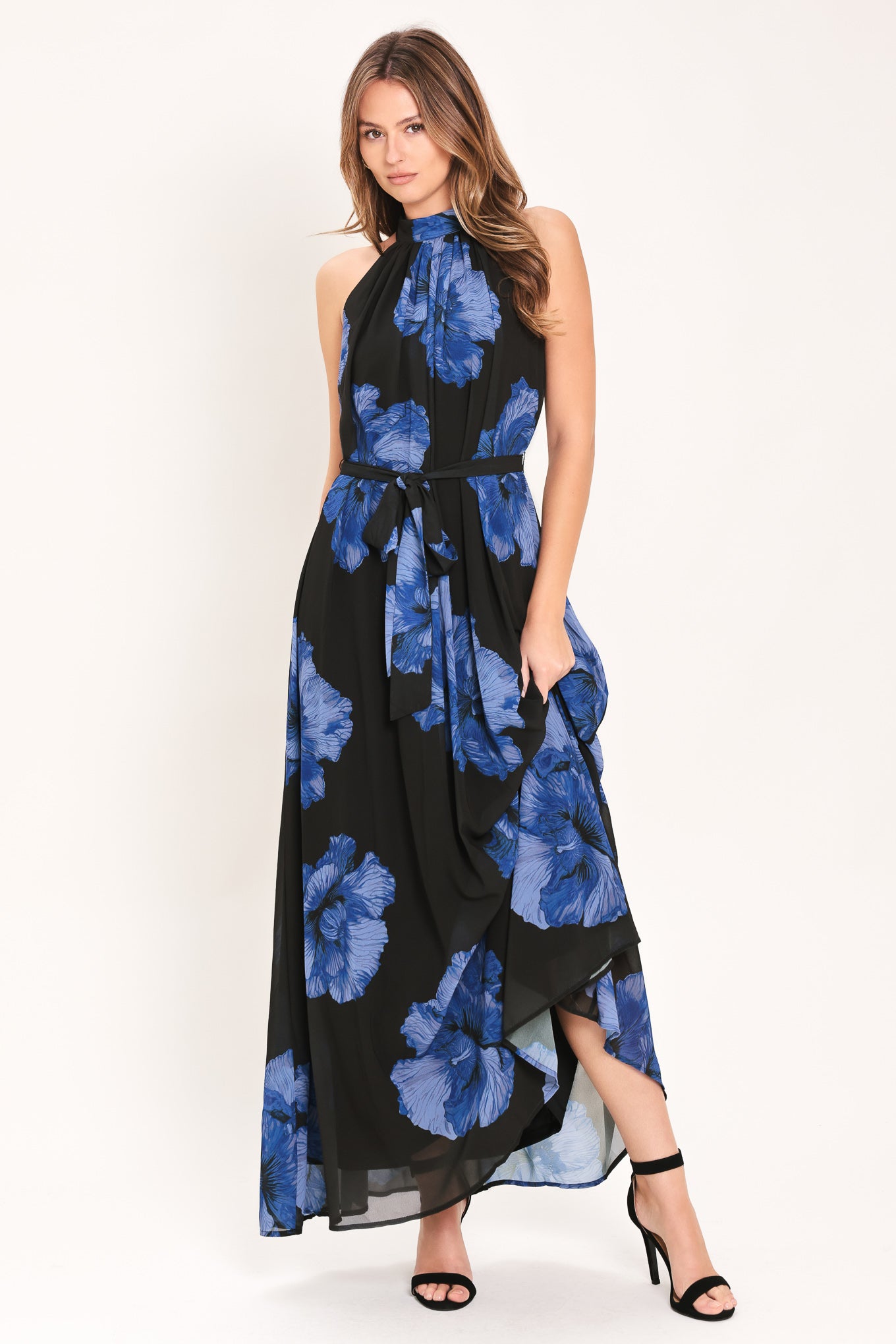 Woman wearing a black maxi dress with blue floral pattern, back neck button closure, and self sash tie | Flying Tomato
